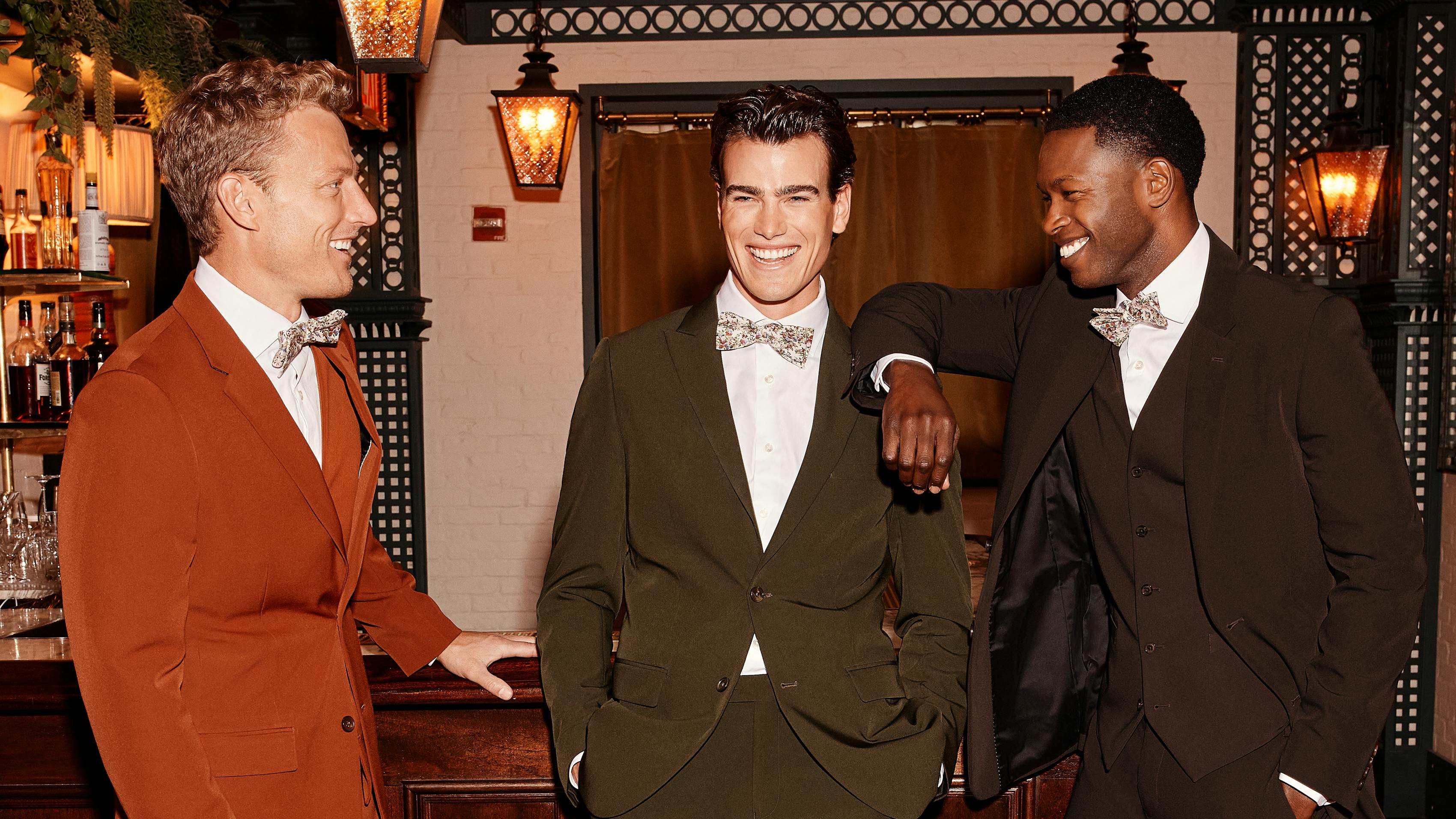 Three men wearing a clay suit, olive suit, and chocolate brown suit as wedding guests