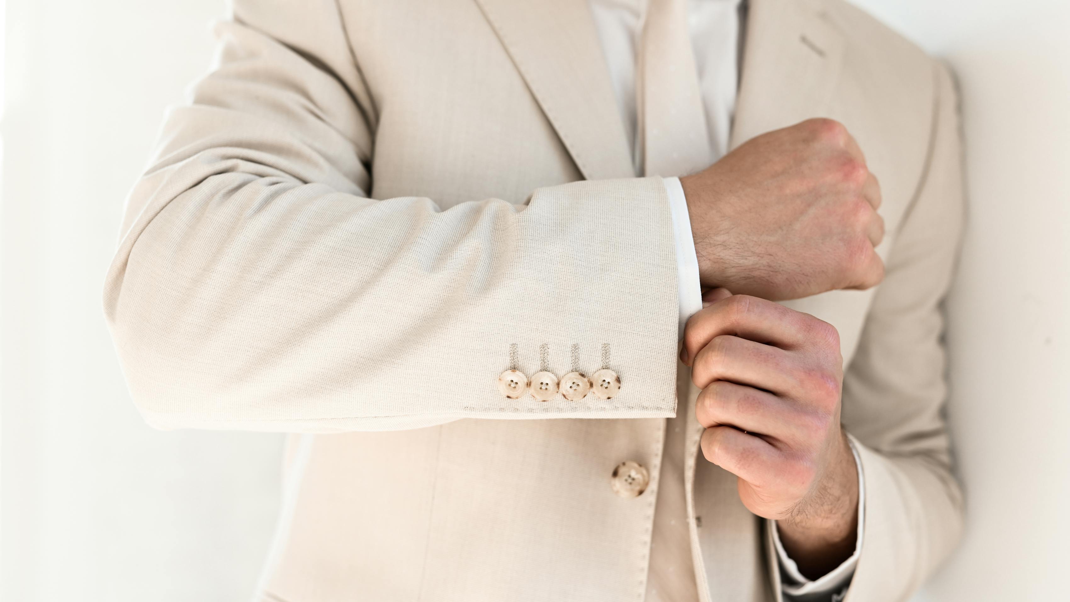 Adjusting sleeves on tan linen suit for men at a wedding