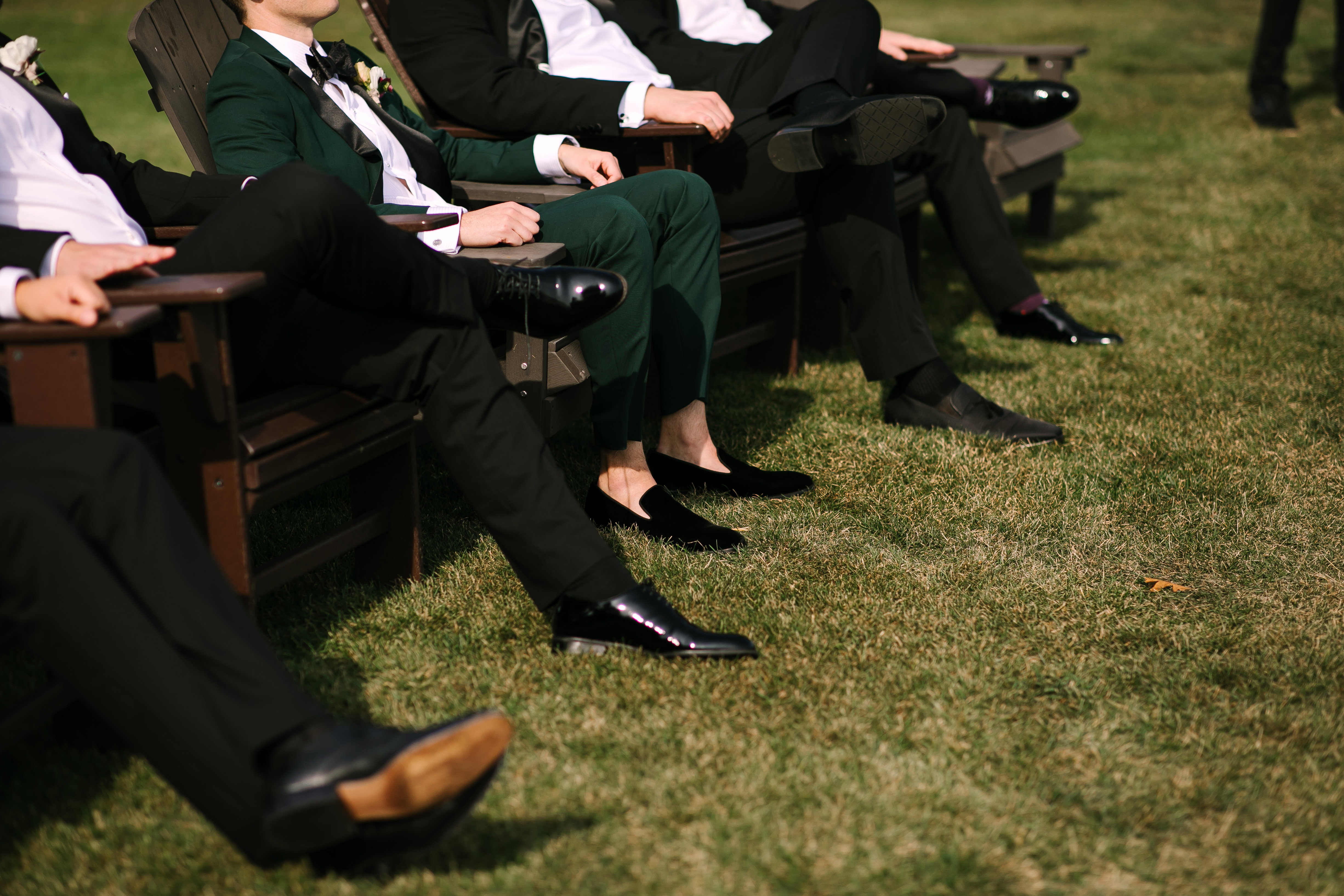 Groom wearing green tuxedo and guests wearing men's black tie outfits at outdoor wedidng