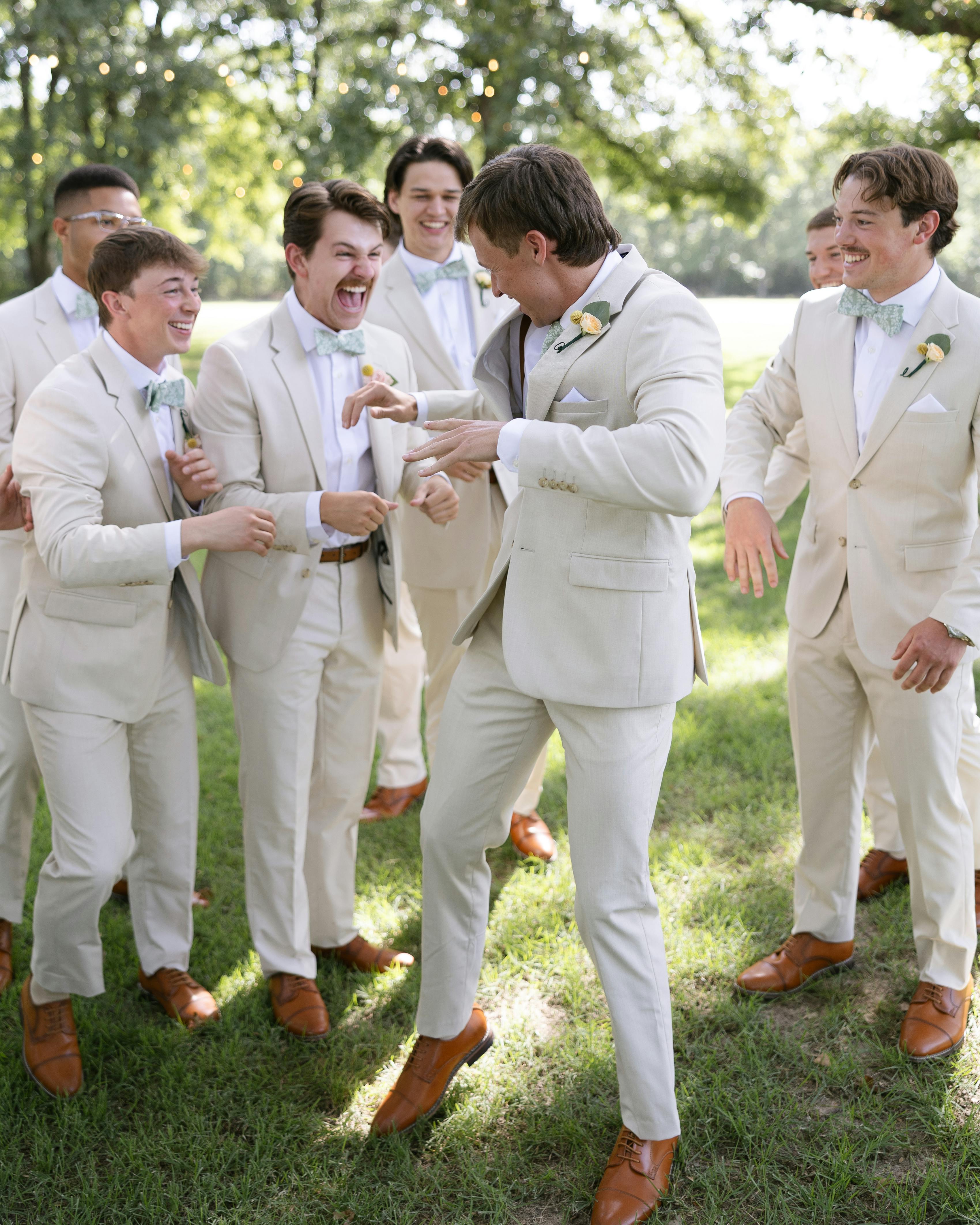 Group of groomsmen laughing wearing light tan wedding suits and blue bow ties