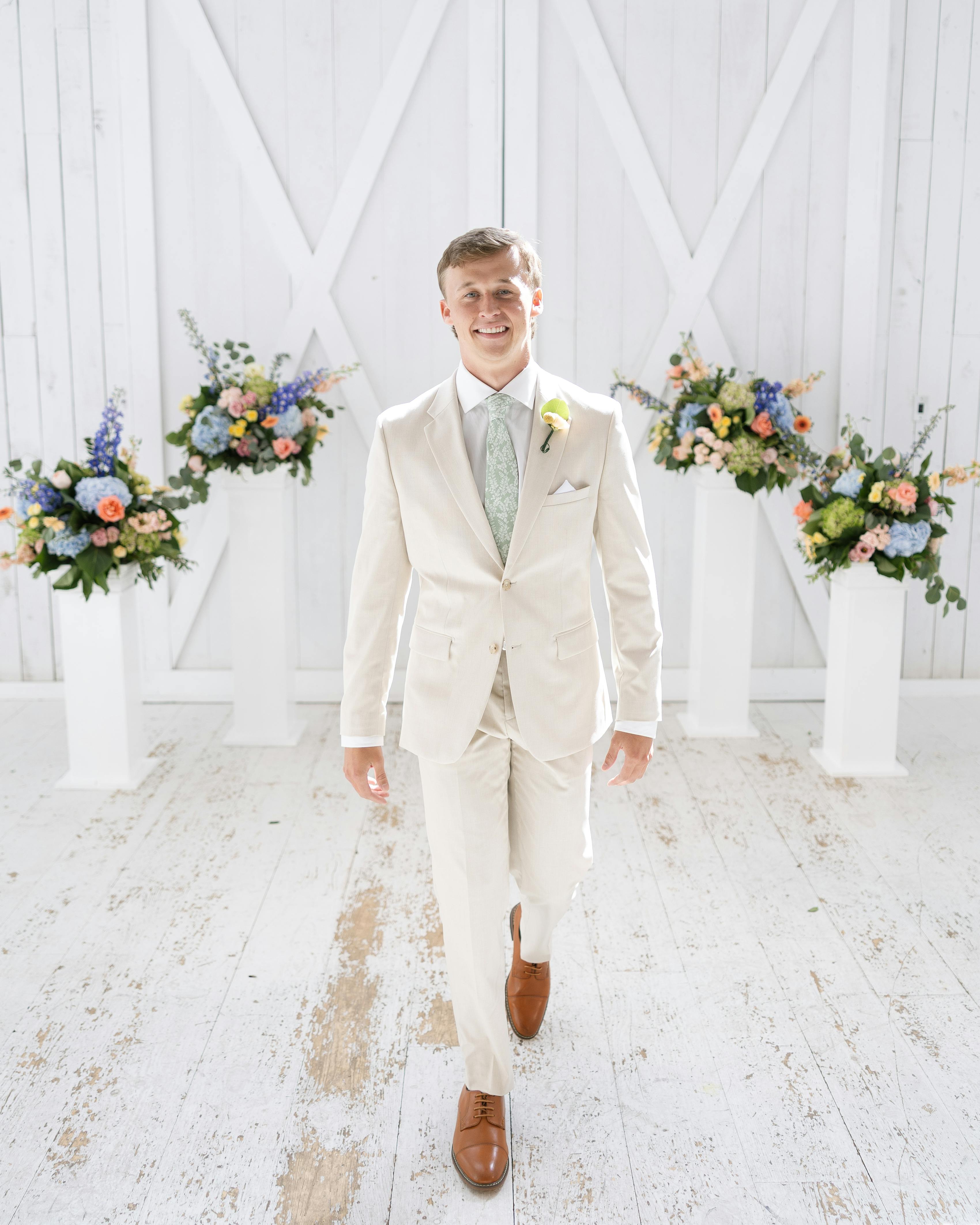 Rustic groom walking down the aisle wearing tan wedding suit with sage green tie
