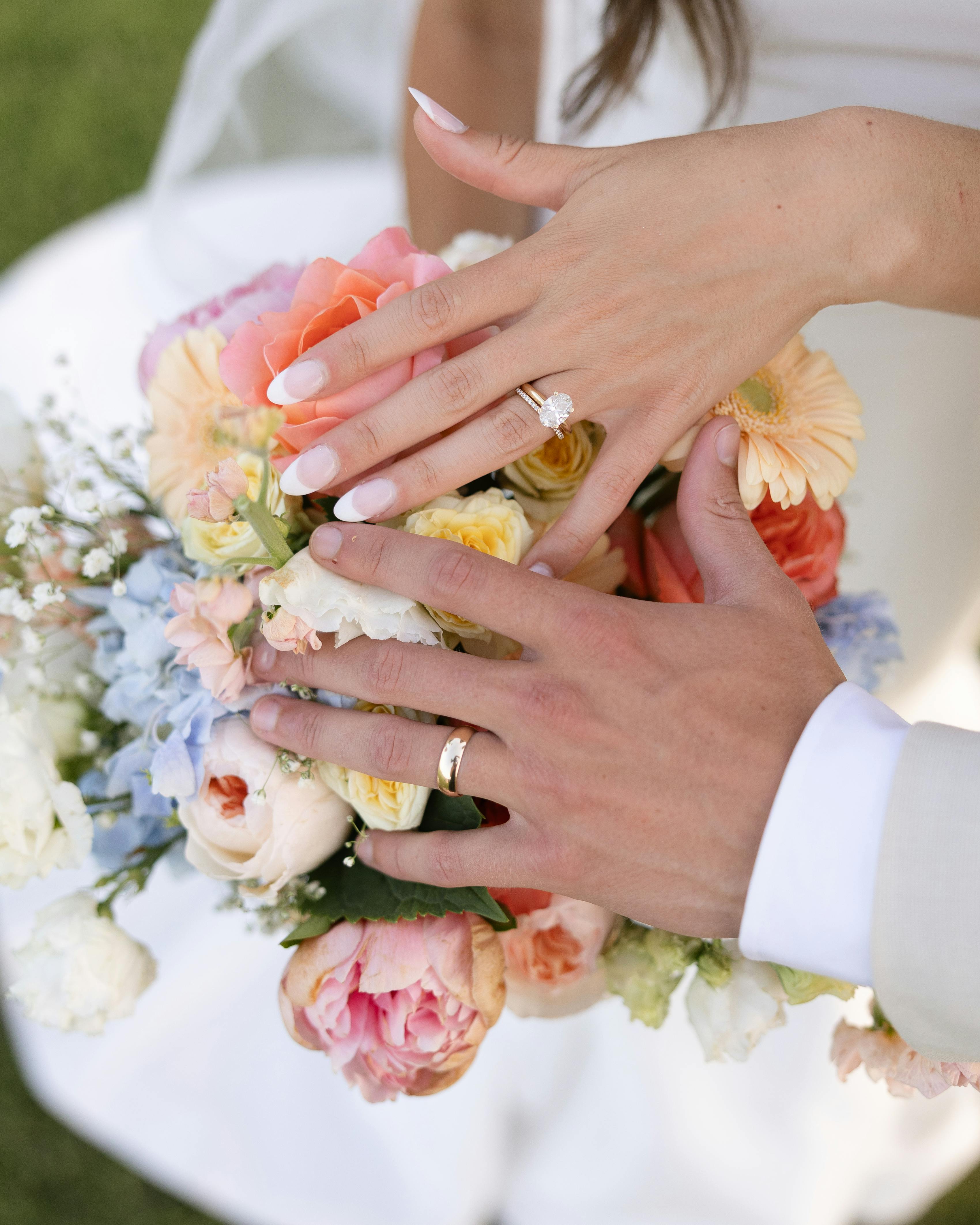Newlywed bride and groom showing off wedding rings over colorful pastel florals