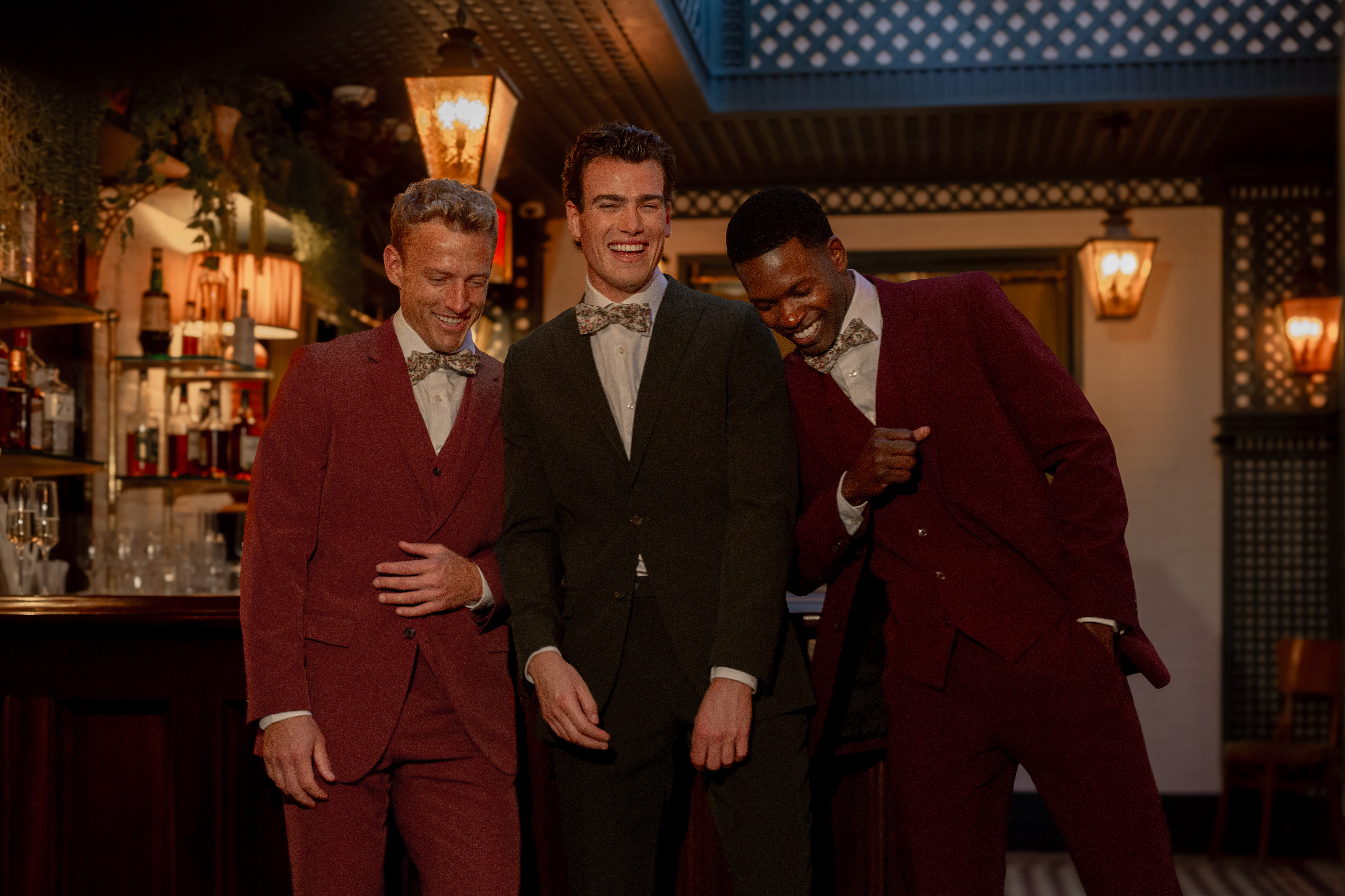 Guy friends wearing jewel tone suits at bar for men's holiday party outfits