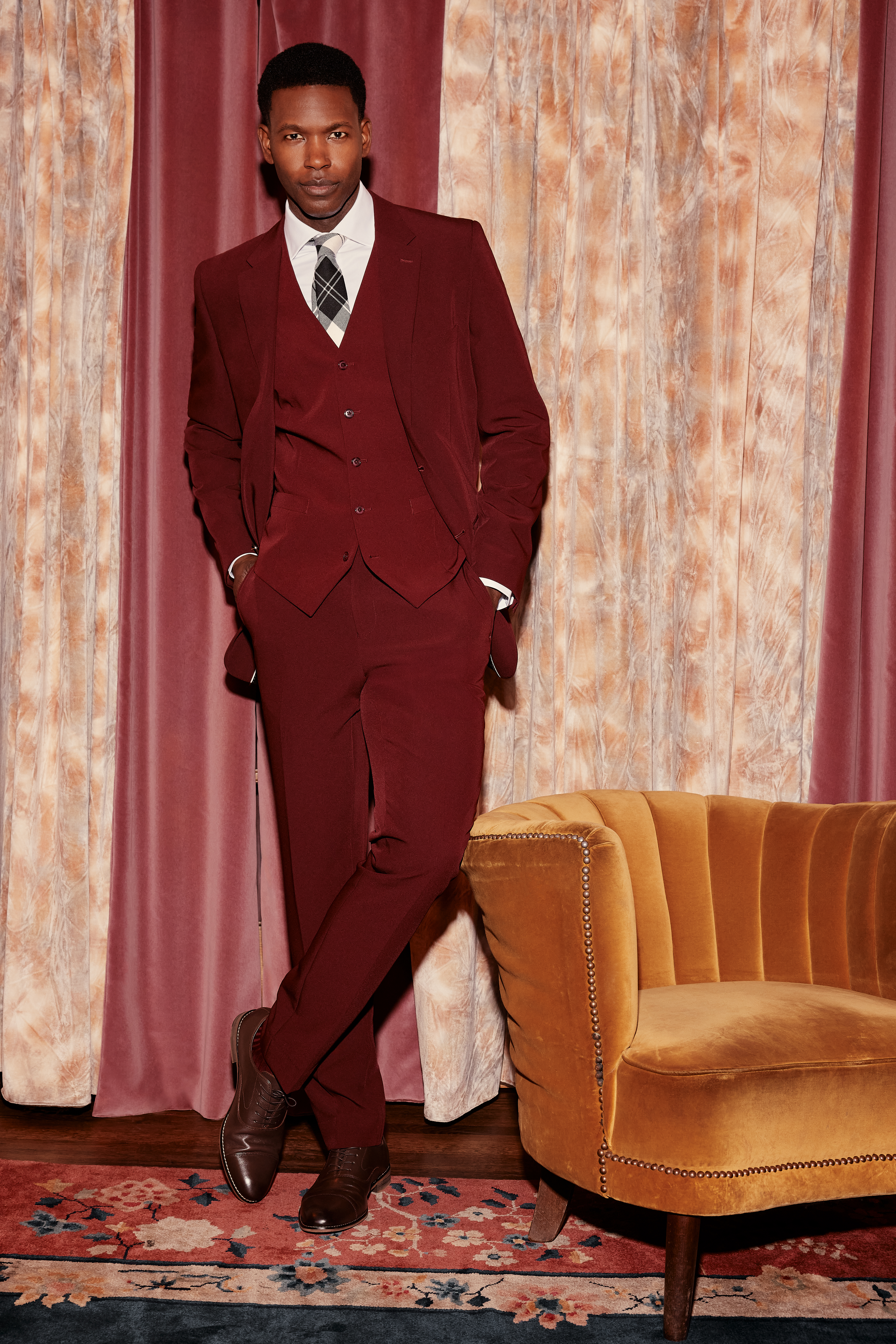 Man wearing 3-piece dark red suit with plaid tie at swanky velvet cocktail hour