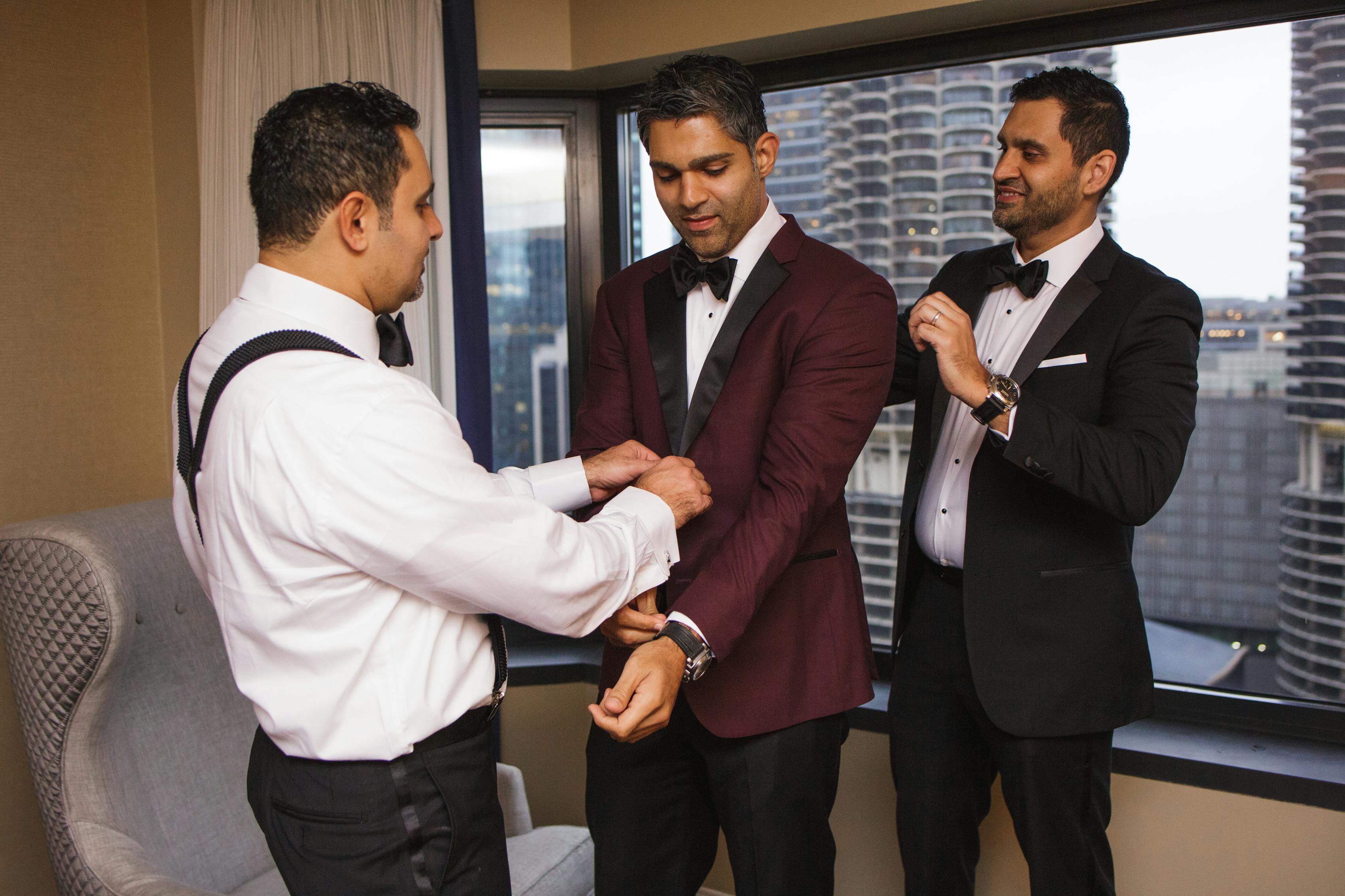 Groom wearing burgundy tuxedo getting ready with groomsmen in black tuxedos for winter wedding
