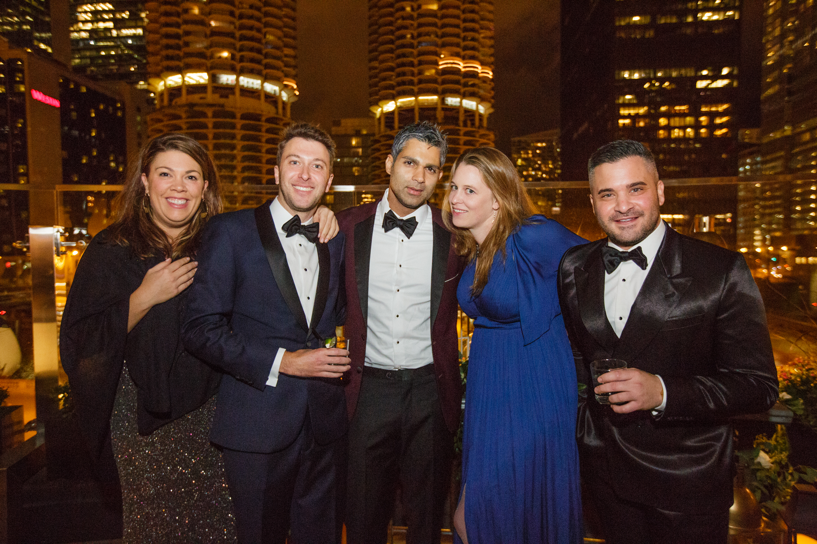 Men and women wearing trendy holiday party outfits with jewel tone suits and velvet tuxedo