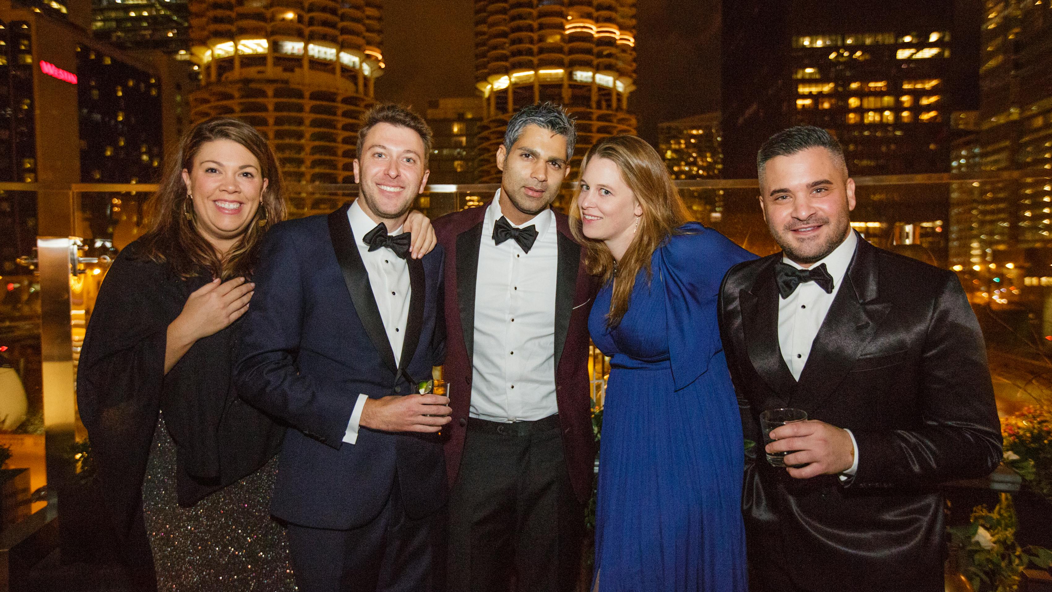 Men and women wearing trendy holiday party outfits with jewel tone suits and velvet tuxedo