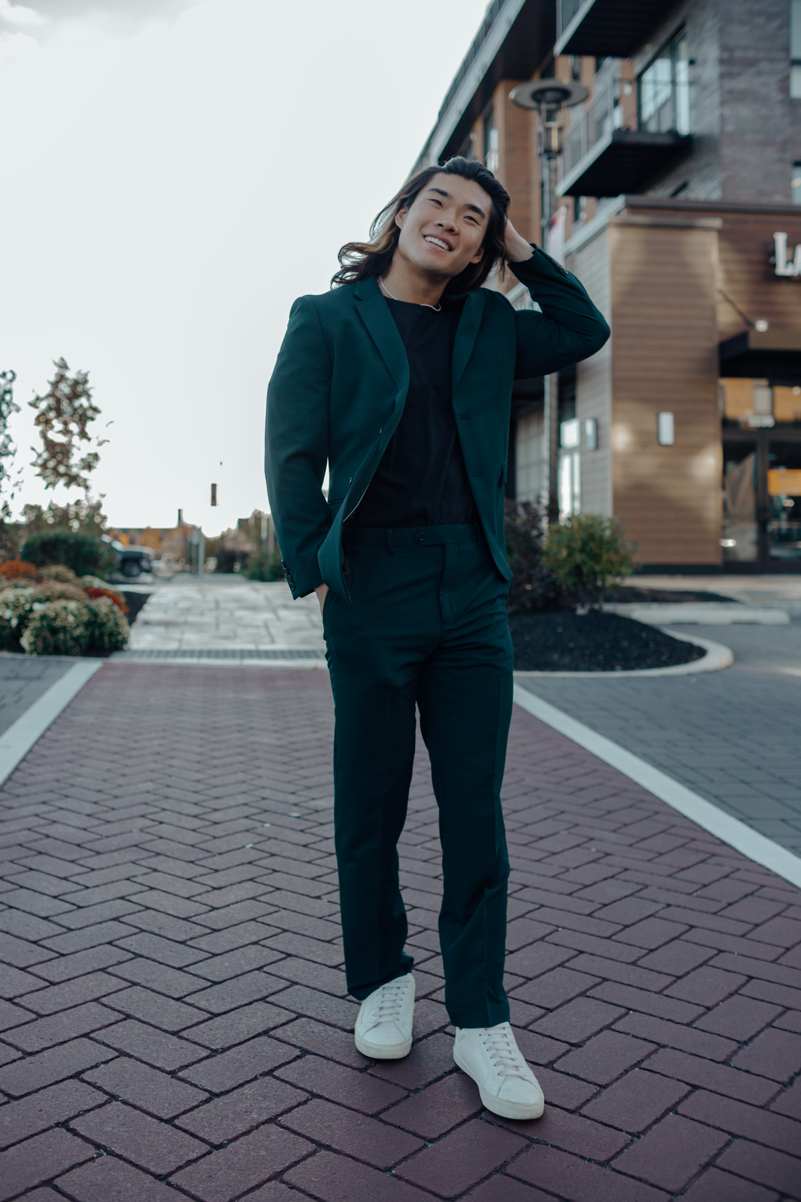 Man wearing casual suit outfit with dark green suit, black tshirt, and white sneakers