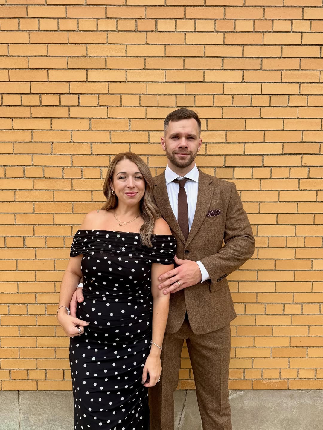 Couple dressed for rehearsal dinner wearing black and white polka dot dress and brown tweed suit