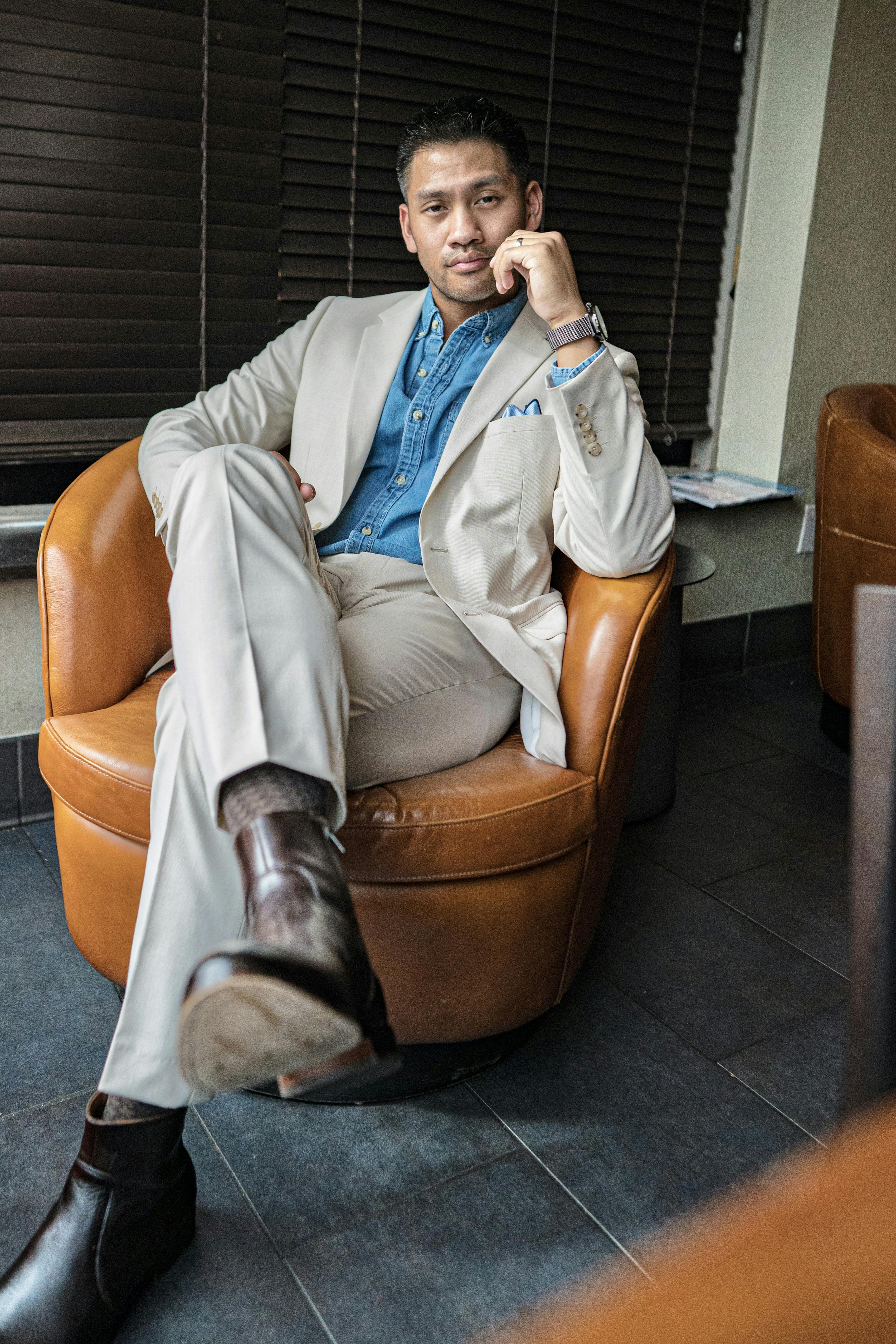 Man wearing casual tan suit for rehearsal dinner with denim shirt and black dress boots