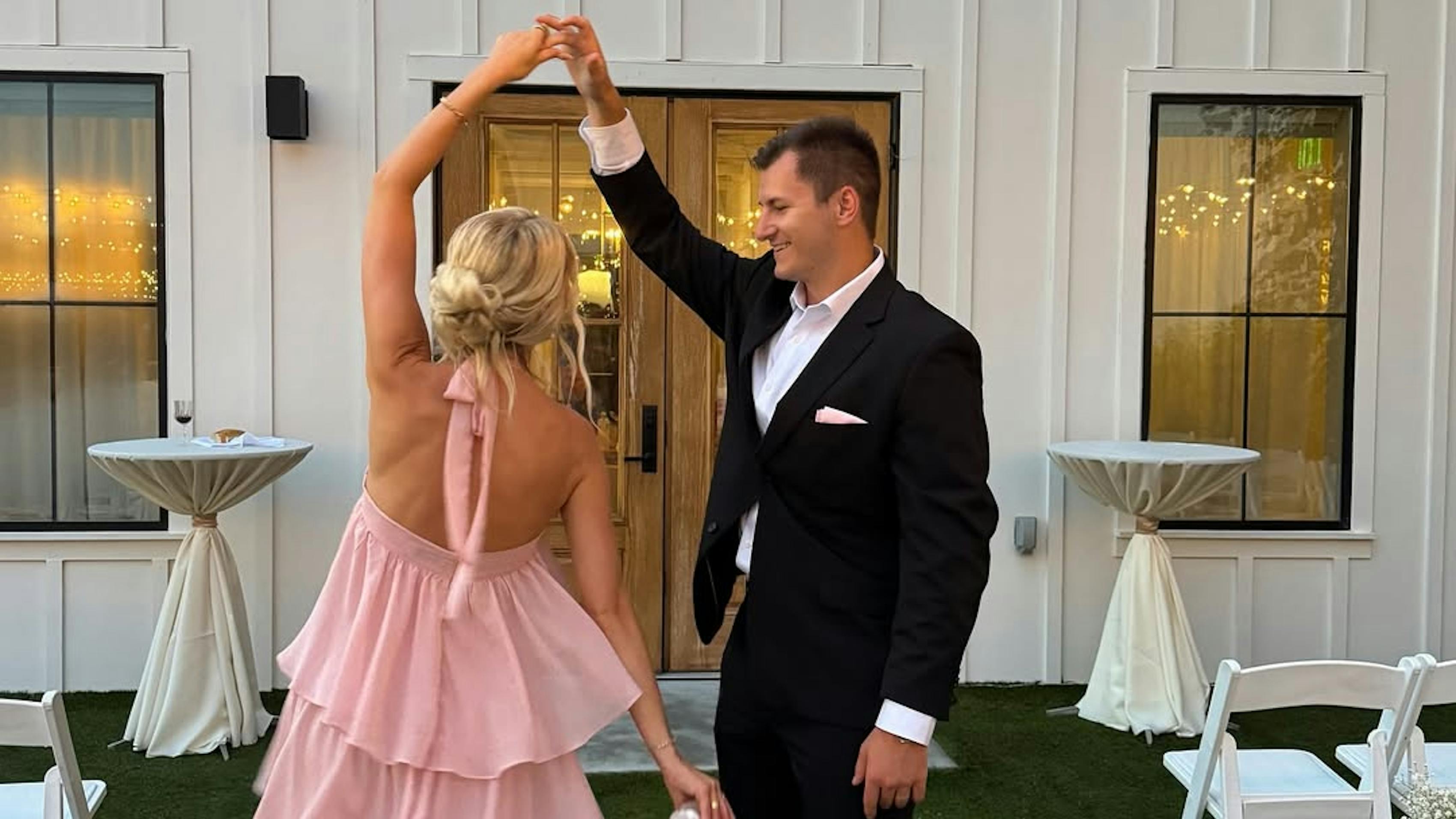 Couple wearing formal rehearsal dinner outfits with pink ruffle halter dress and black suit