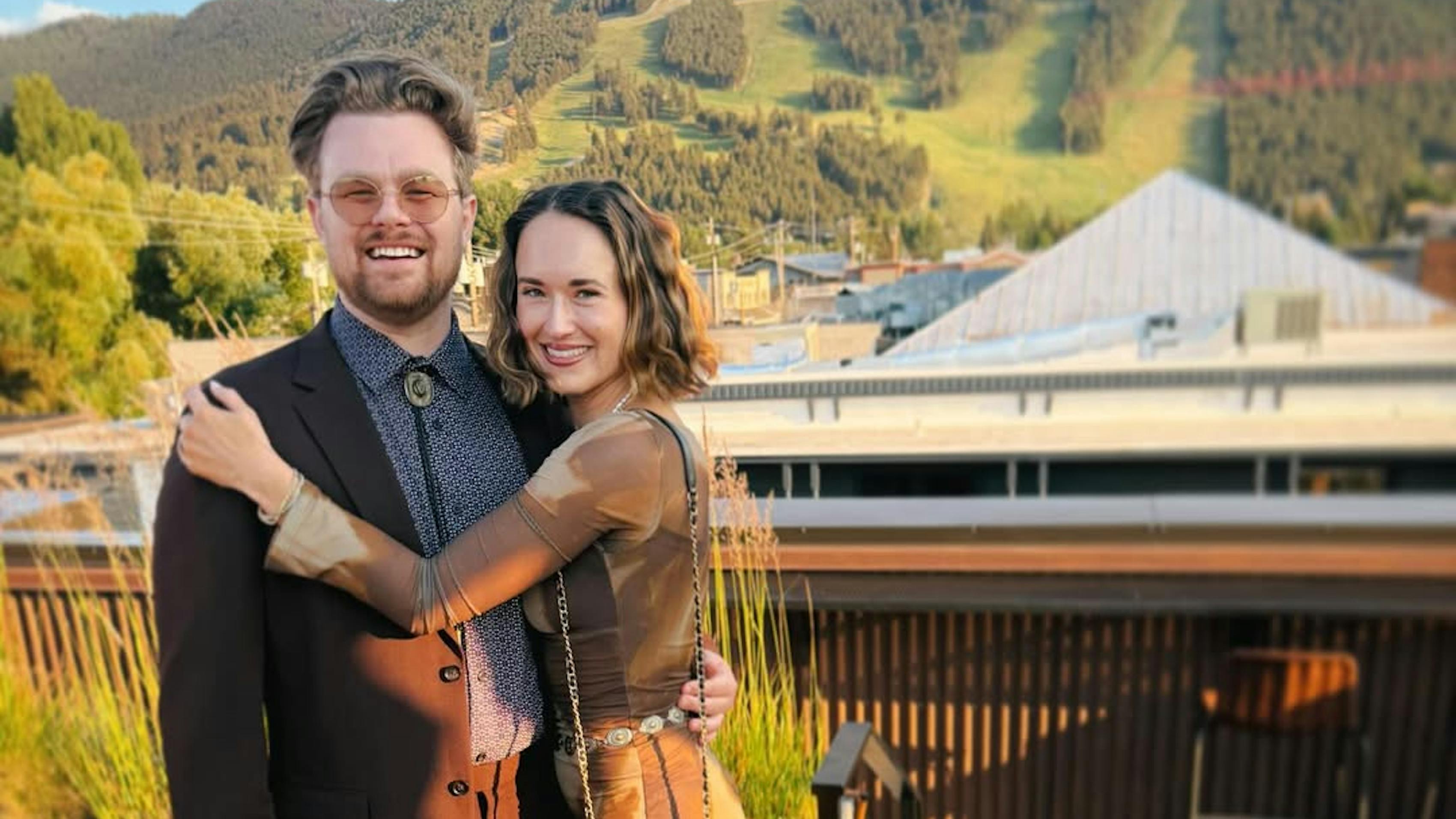 Couple attending mountain rehearsal dinner wearing dark brown suit and bolo tie and brown dress