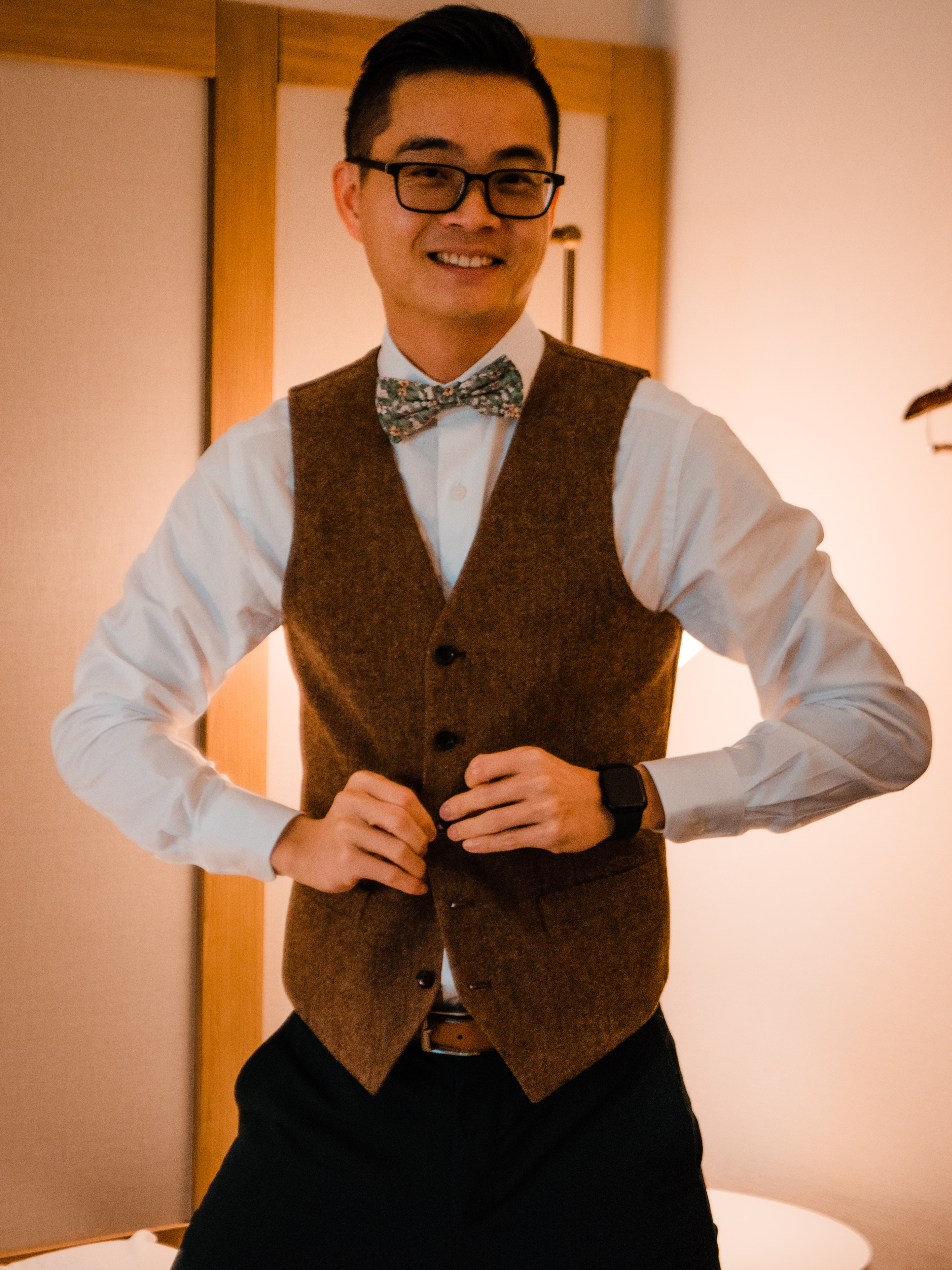 Groom changing into brown tweed suit vest with bow tie after wedding ceremony