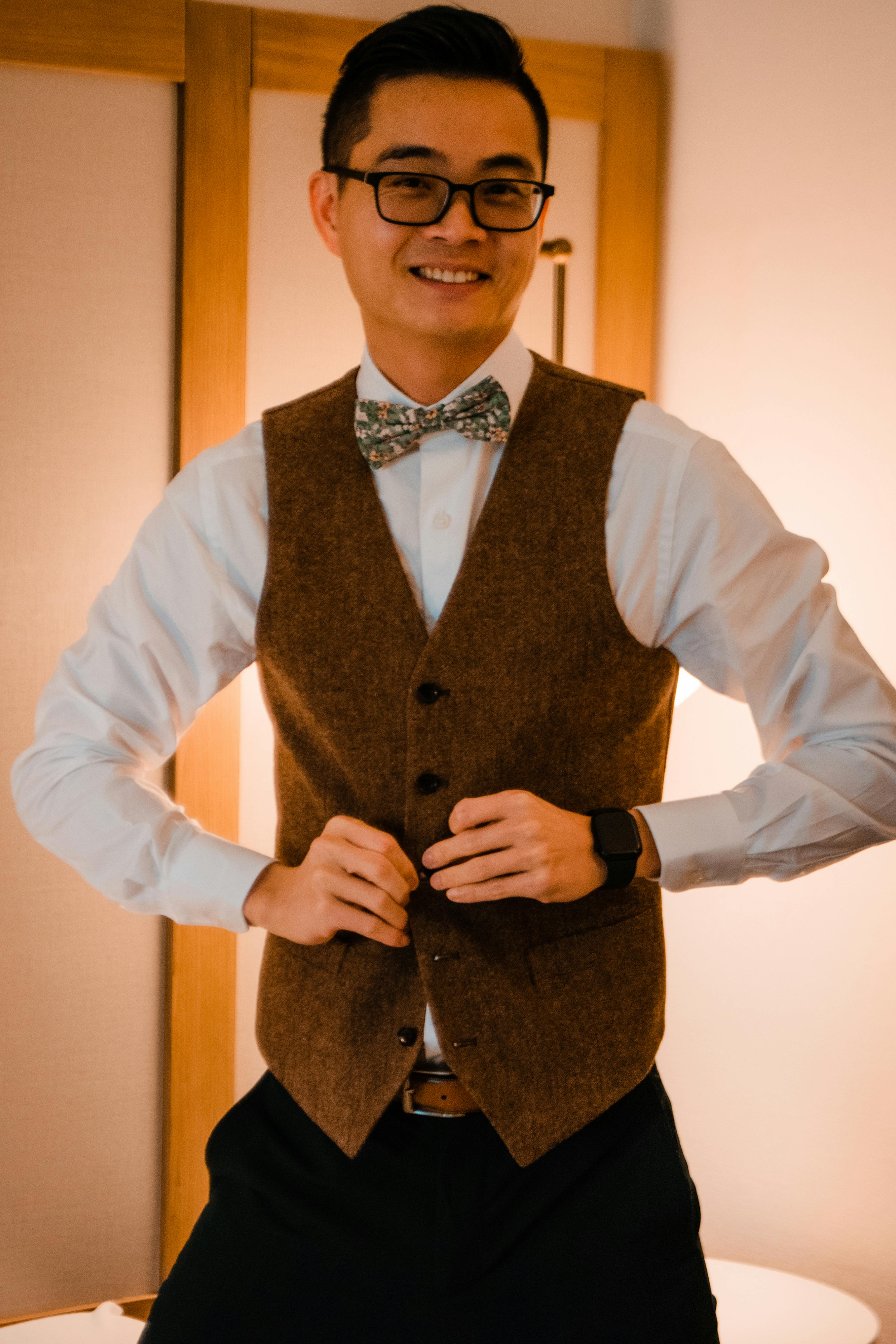 Groom changing into brown tweed suit vest with bow tie after wedding ceremony
