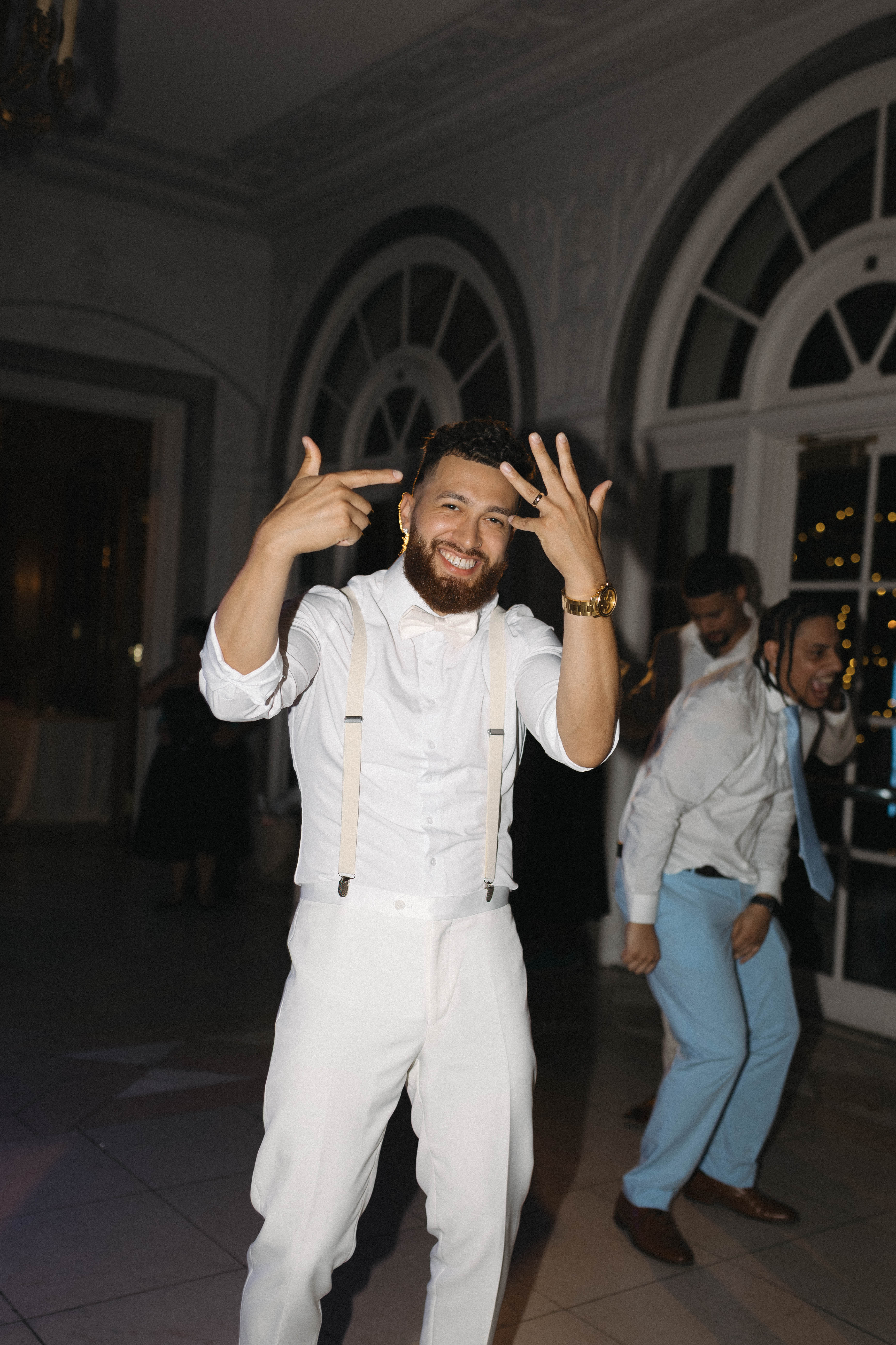 Groom wearing white tuxedo pants with suspenders for wedding reception suit outfit