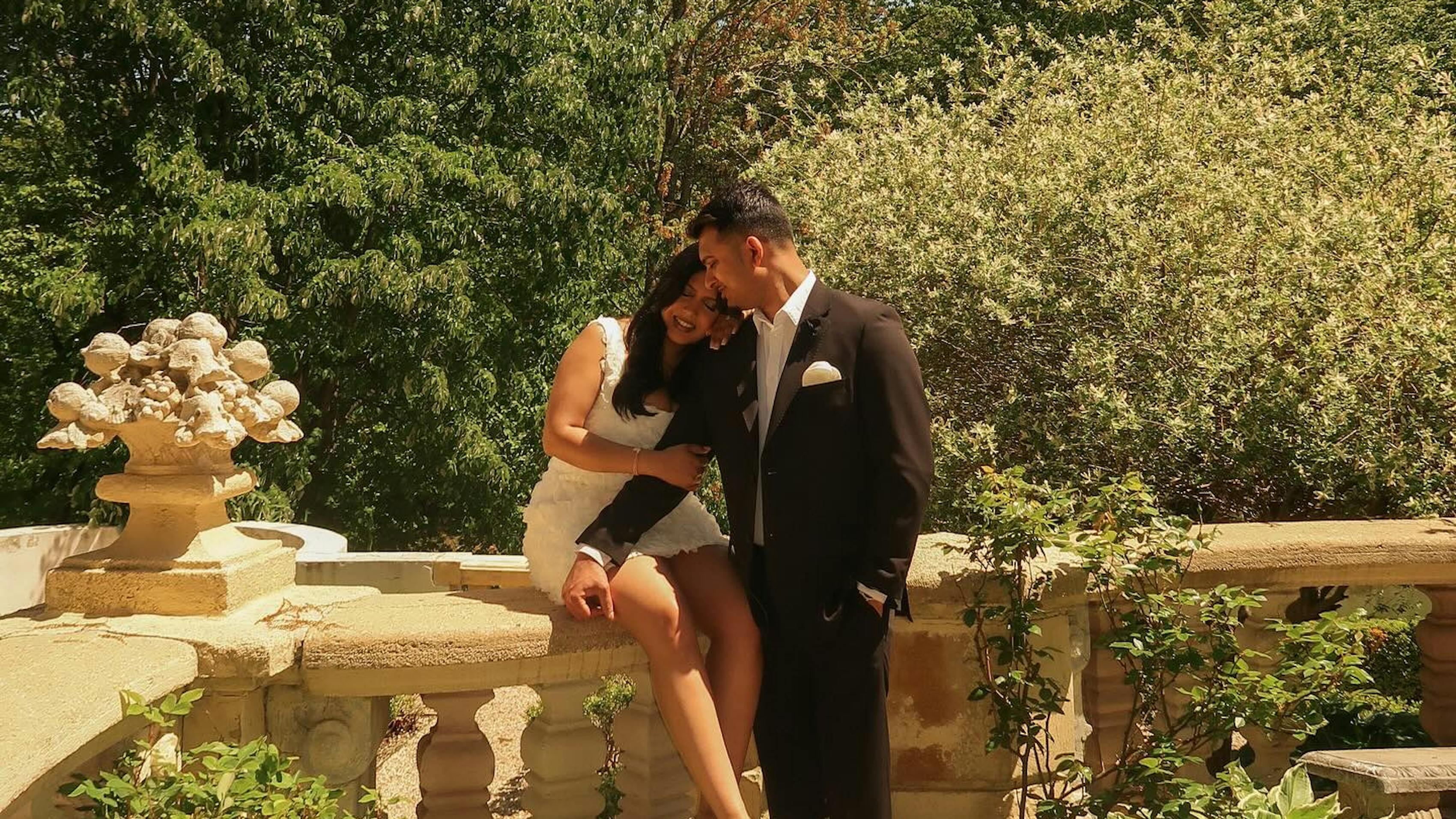 Bride wearing short white dress and groom wearing brown suit in garden for welcome party