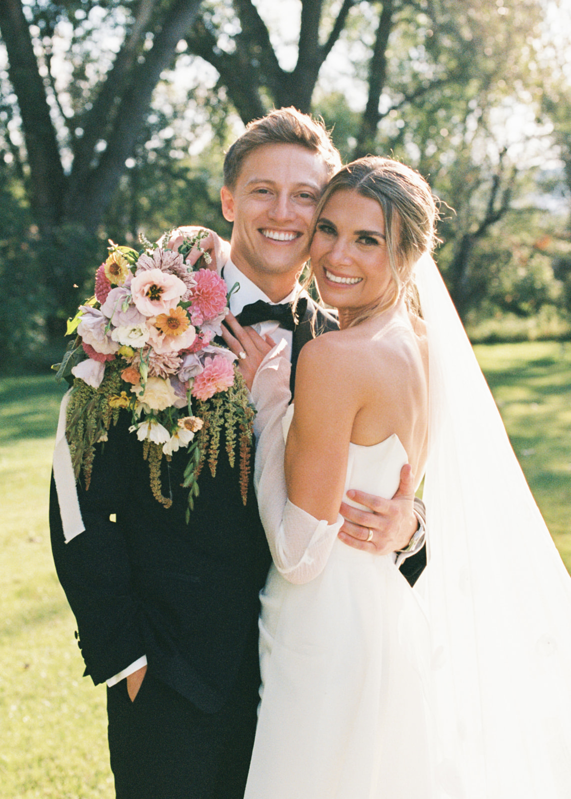 Classic black tie bride and groom wearing tuxedo and gown with pink bouquet at outdoor wedding