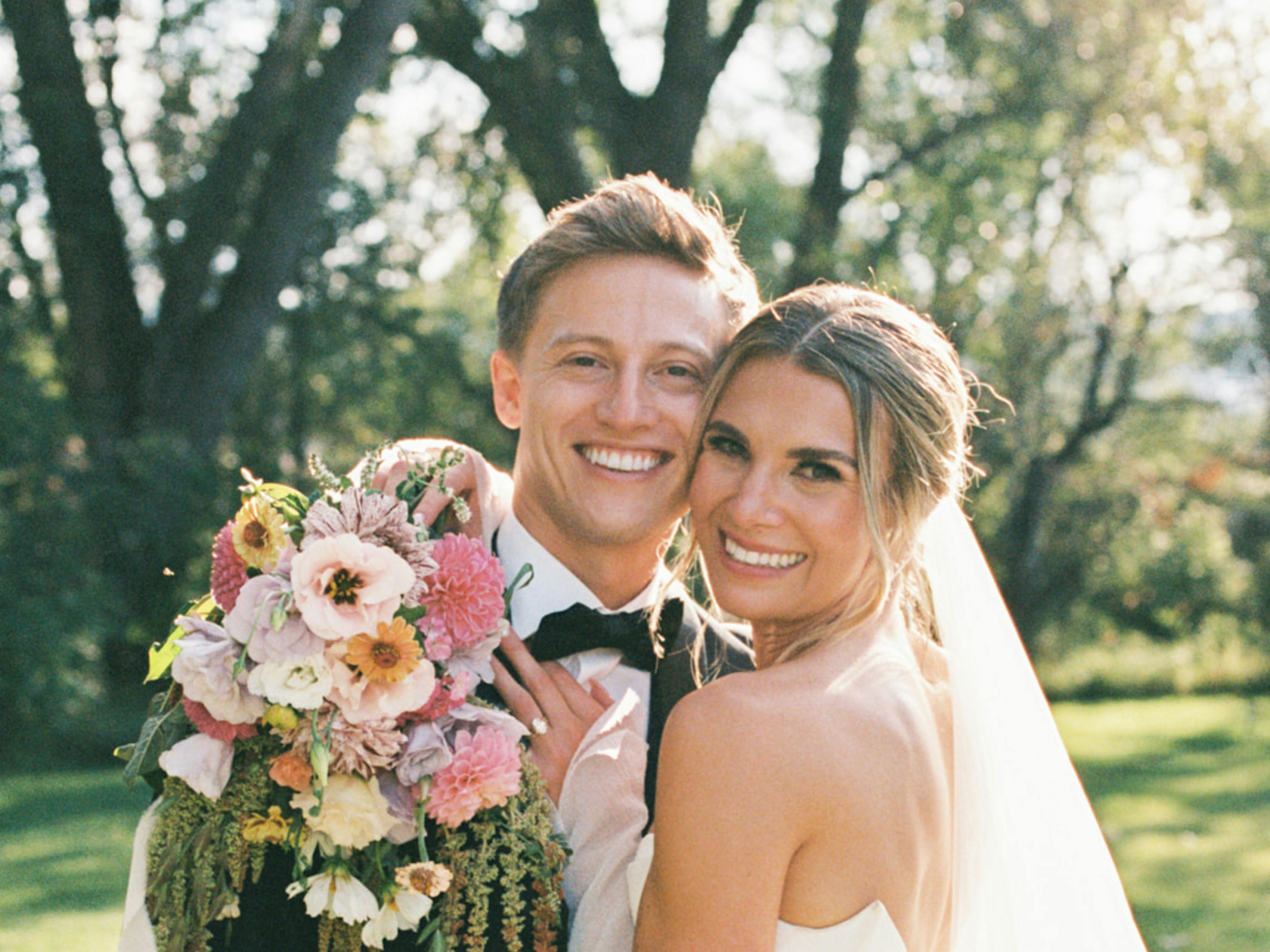 Classic black tie bride and groom wearing tuxedo and gown with pink bouquet at outdoor wedding
