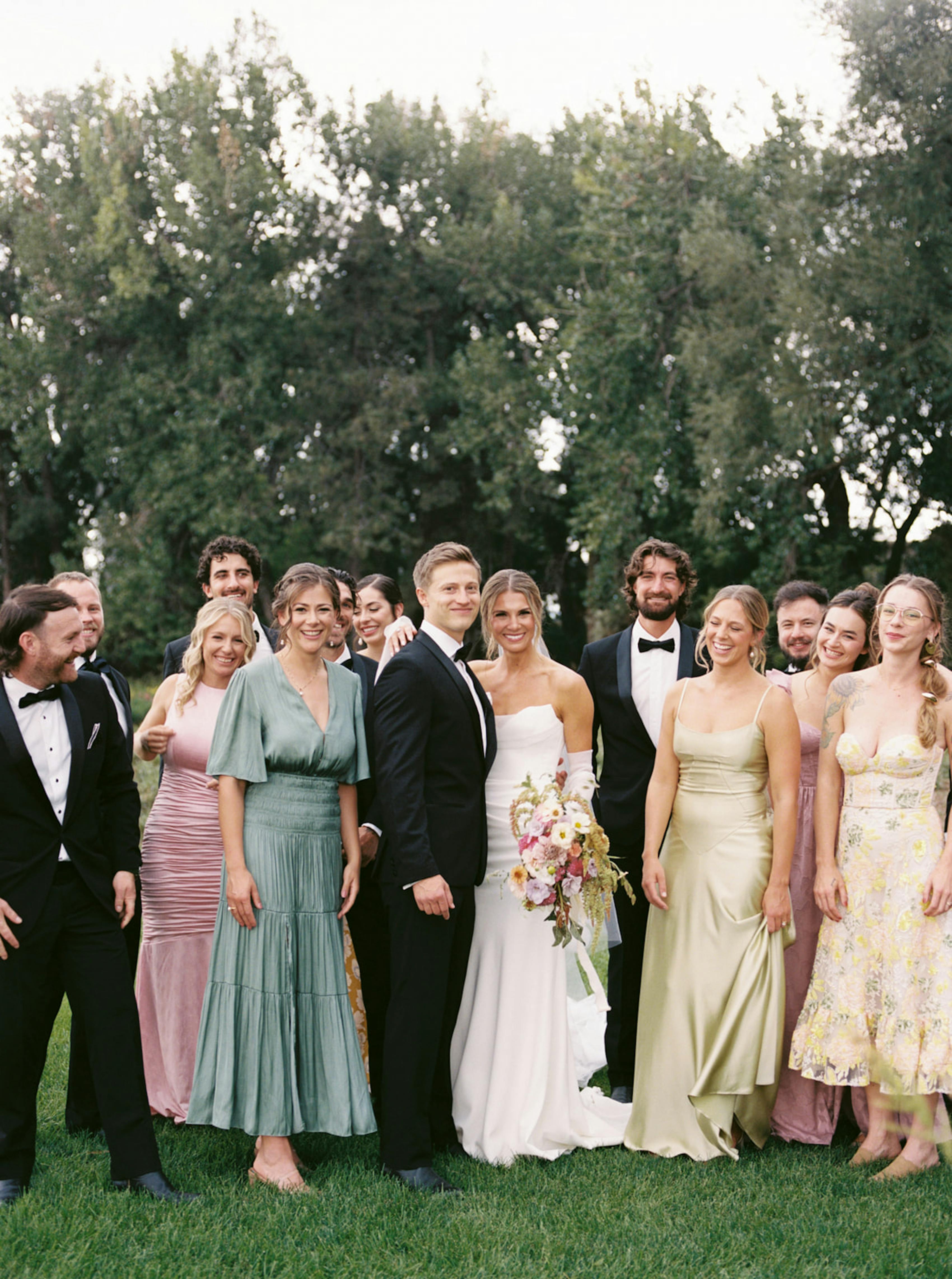 Bridal party at garden wedding with pastel bridesmaids dresses and black tuxedos
