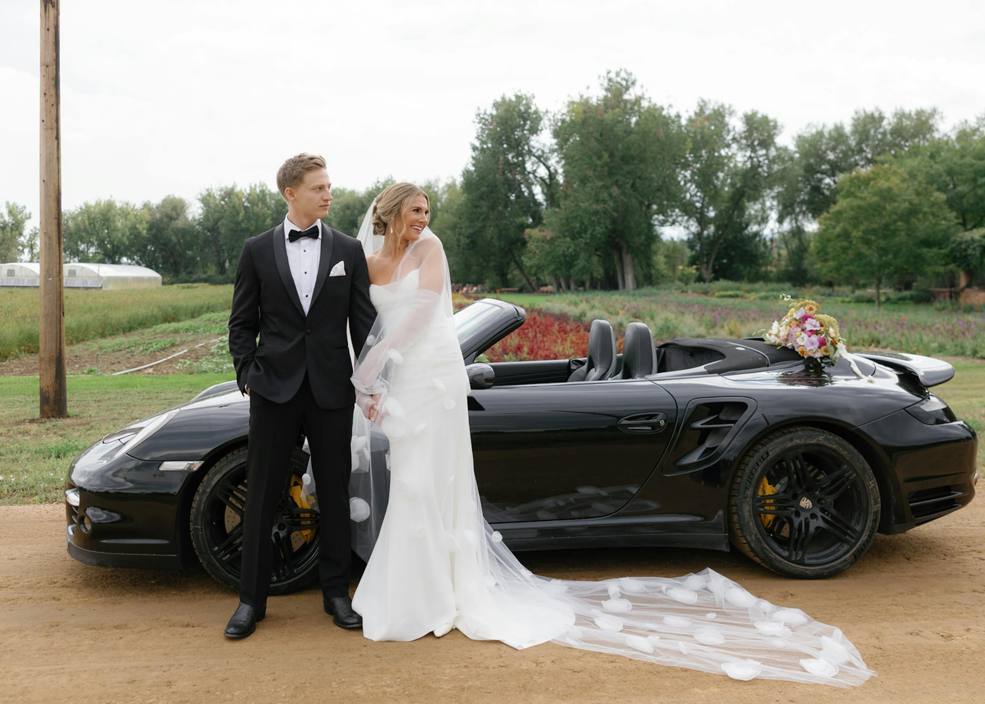 Bride and groom posing with vintage car at garden wedding