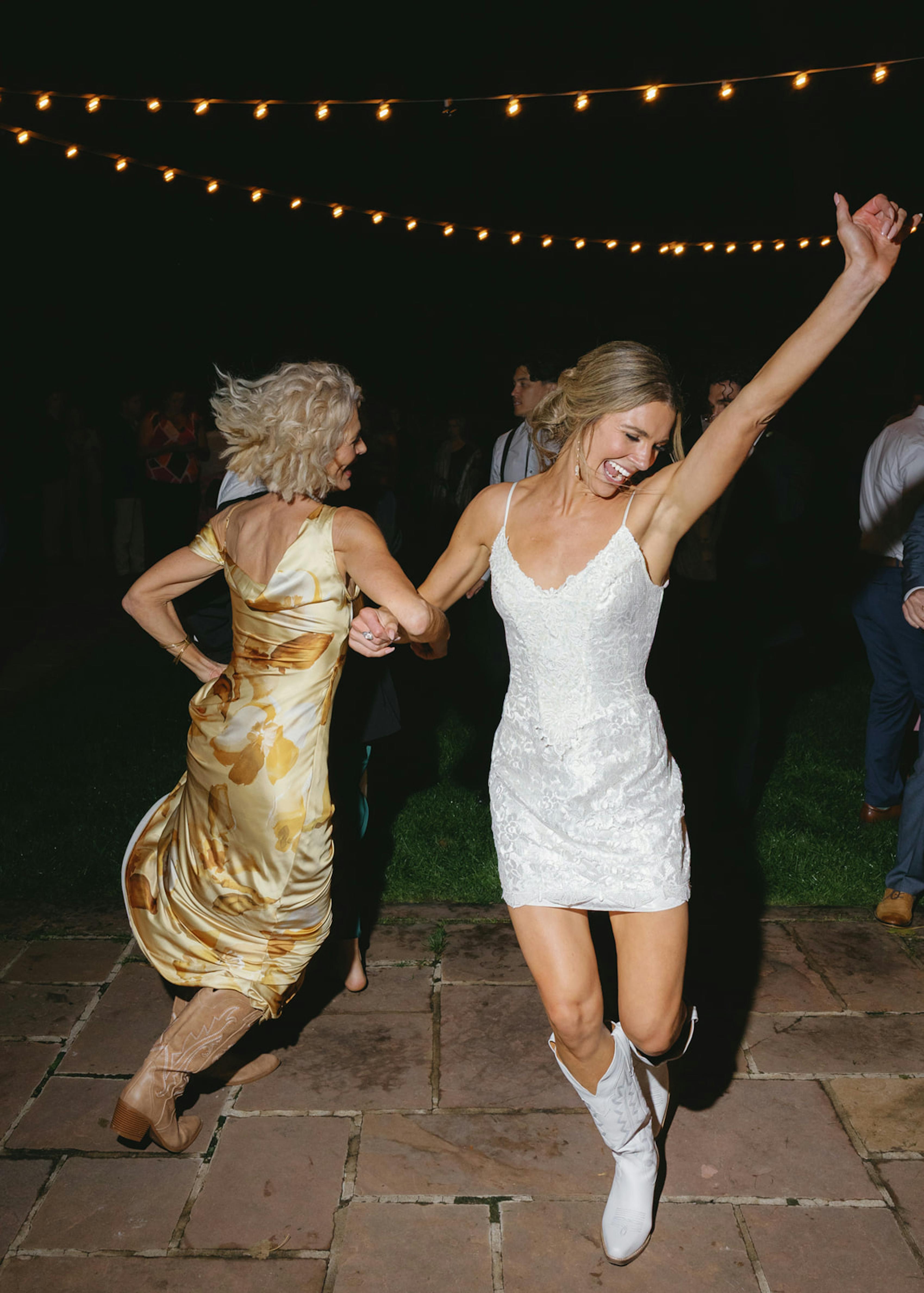 Bride dancing with mother in reconstructed vintage mini wedding dress and cowboy boots