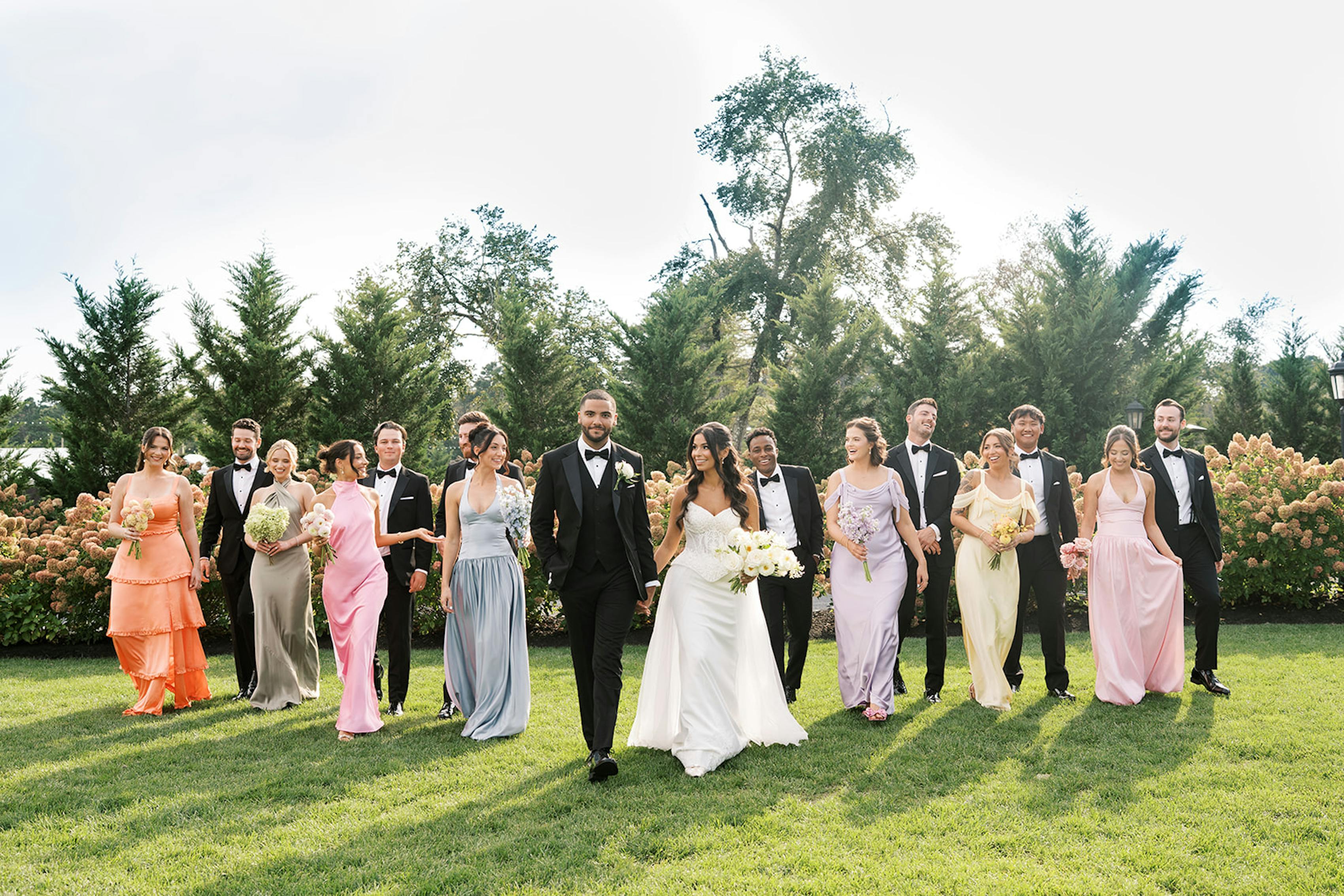 Bridal party wearing pink, sage, and butter yellow dresses with groomsmen wearing tuxedos