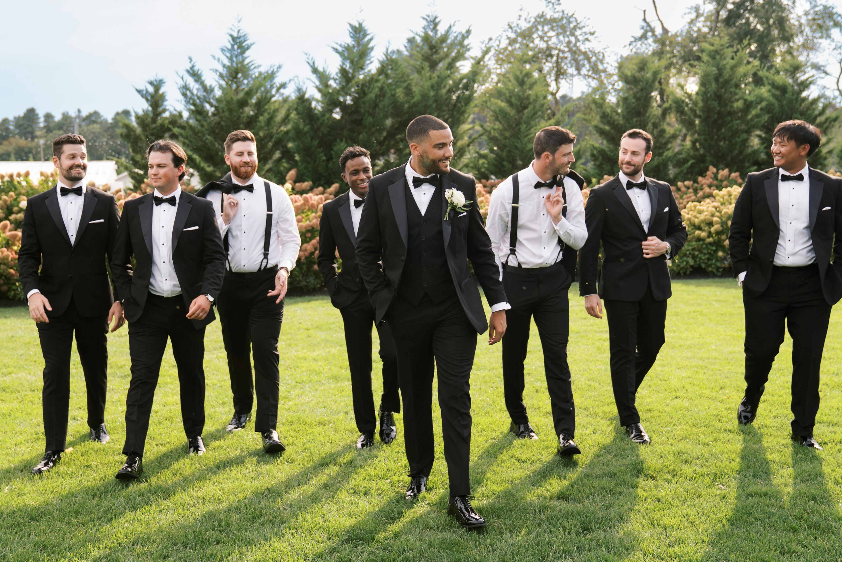 Groomsmen wearing black tuxedos and suspenders waking outside wedding venue
