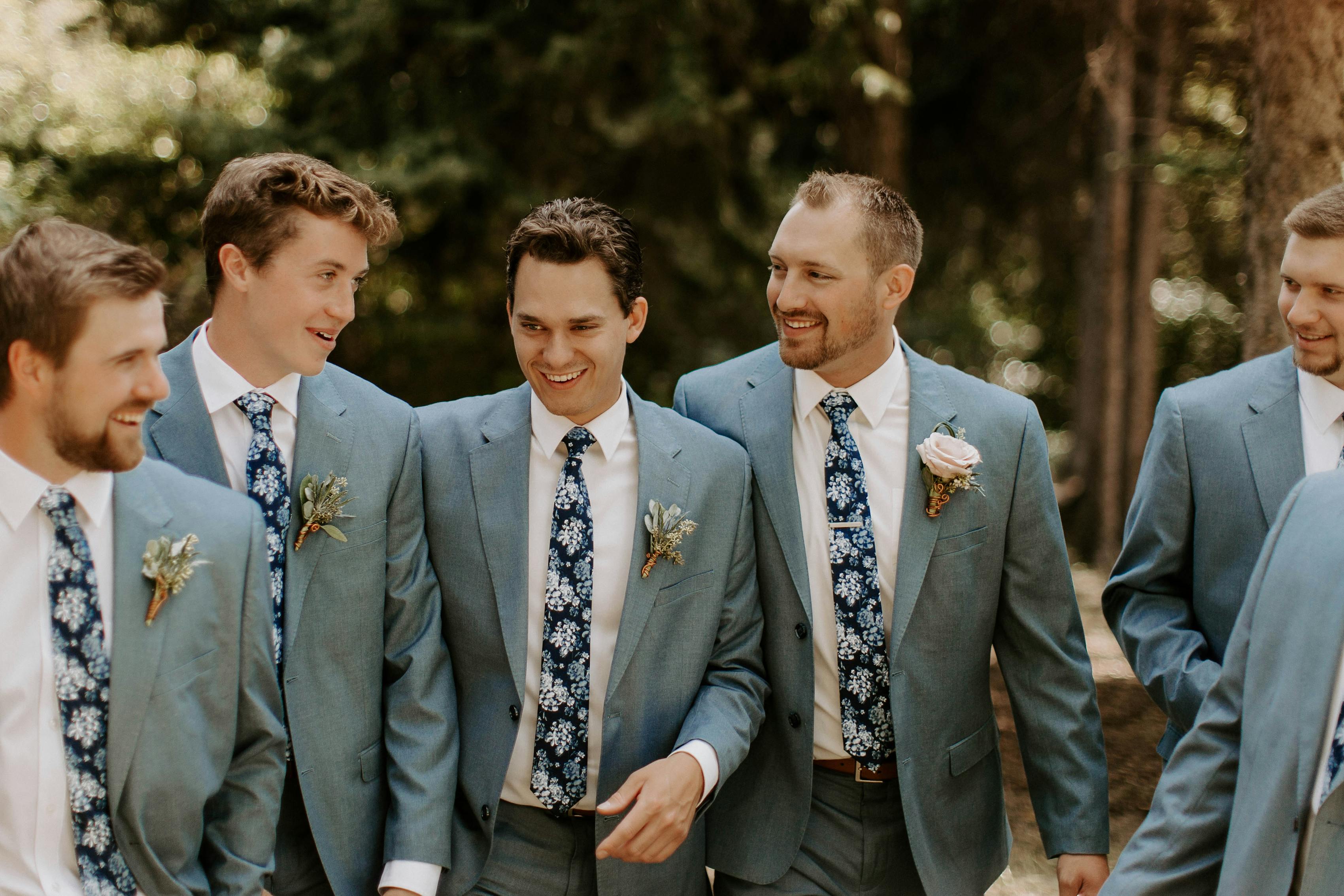 Candid groomsmen laughing wearing light blue suits with blue floral ties