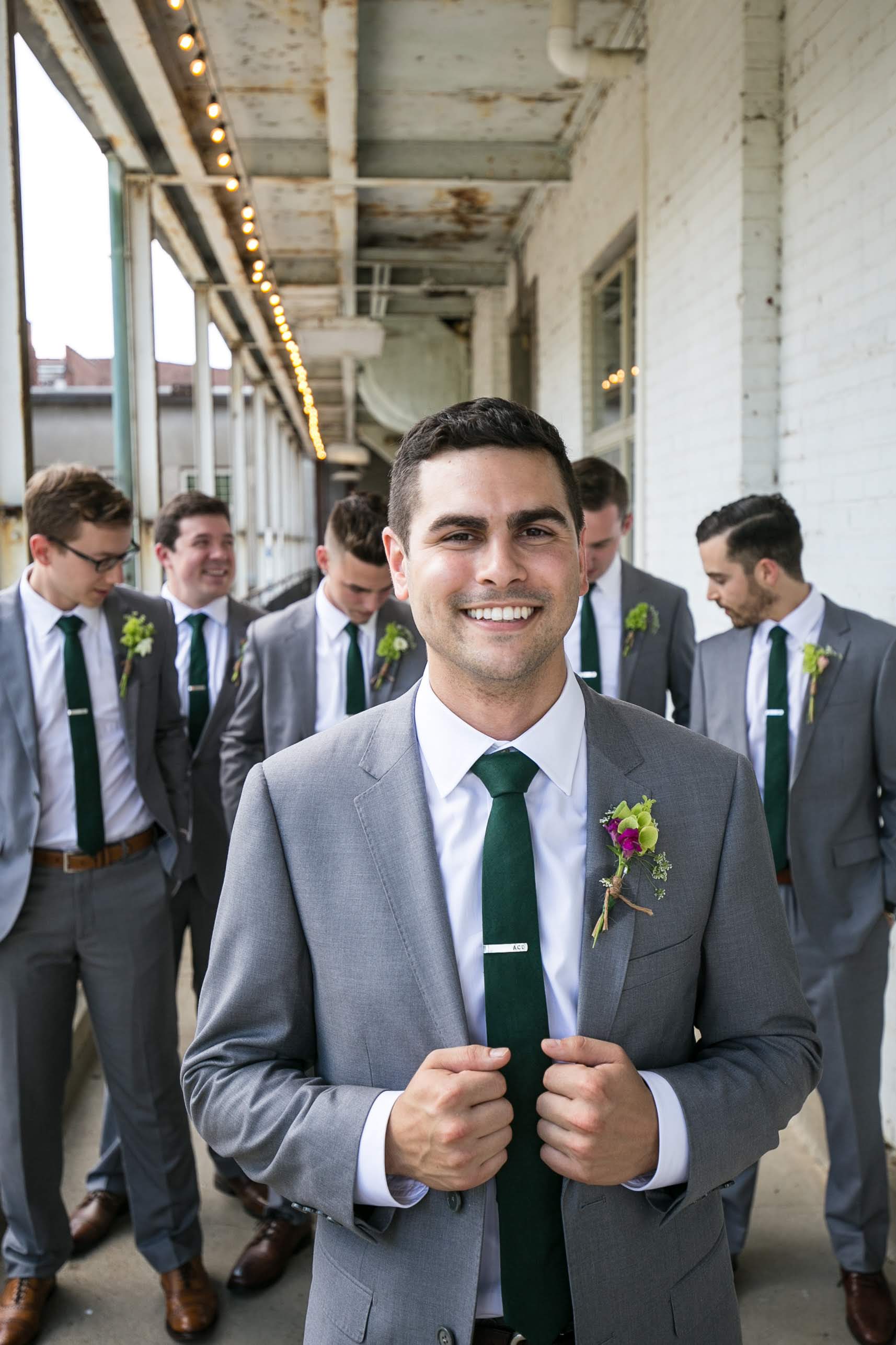 Groom walking in front of groomsmen matching in light grey wedding suits with green ties