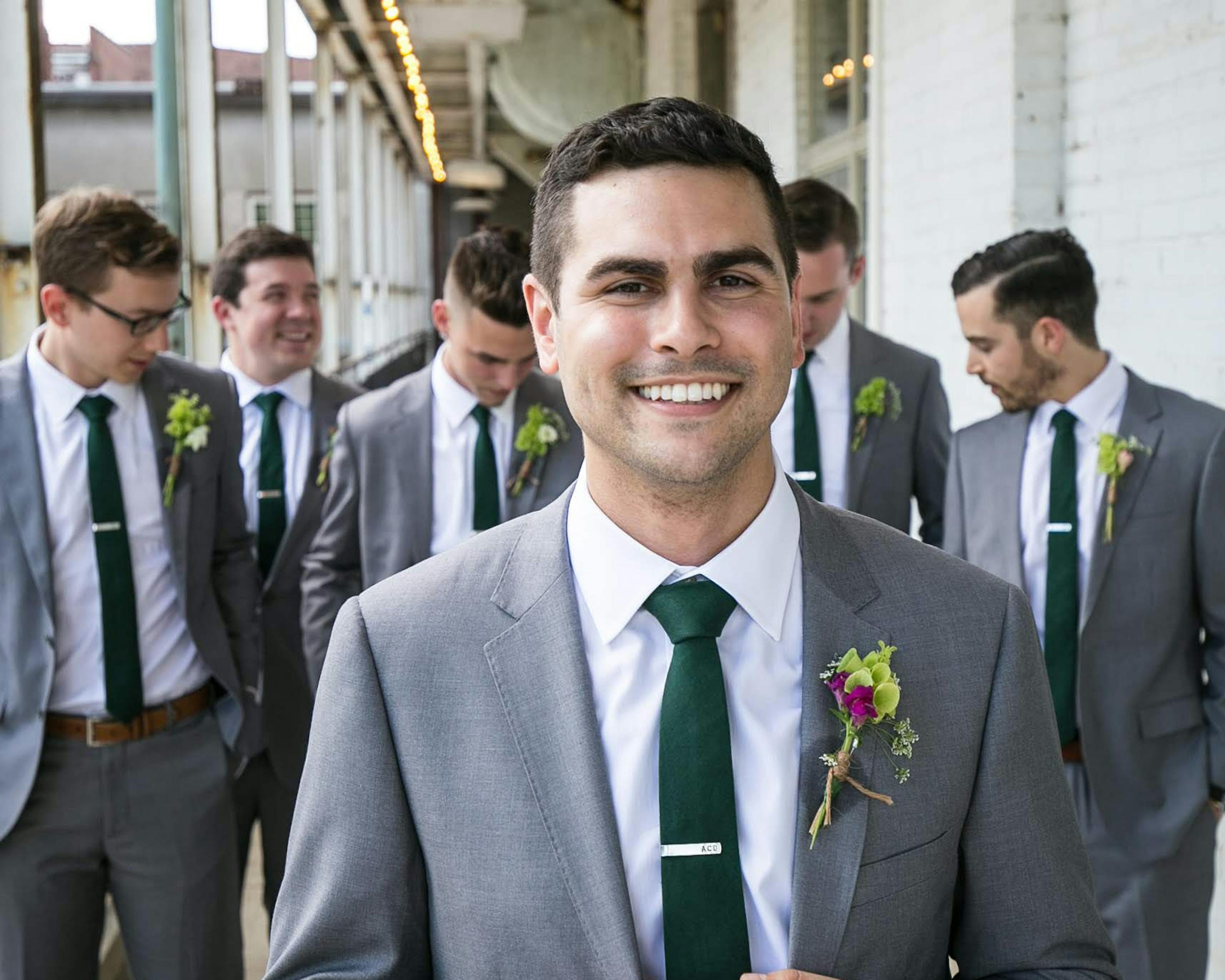Groom walking in front of groomsmen matching in light grey wedding suits with green ties