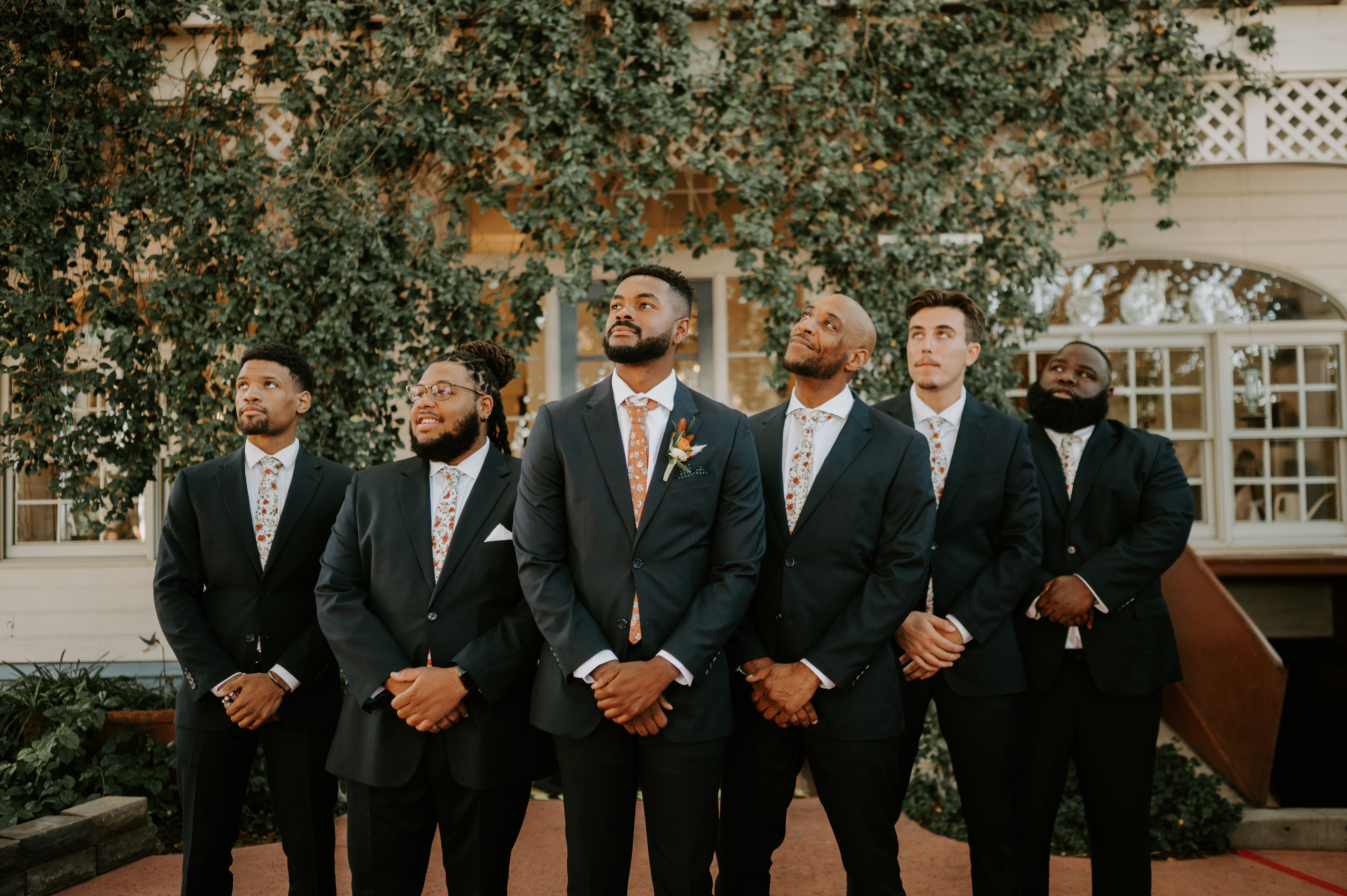 Serious face groomsmen of different heights wearing charcoal grey suits and floral ties