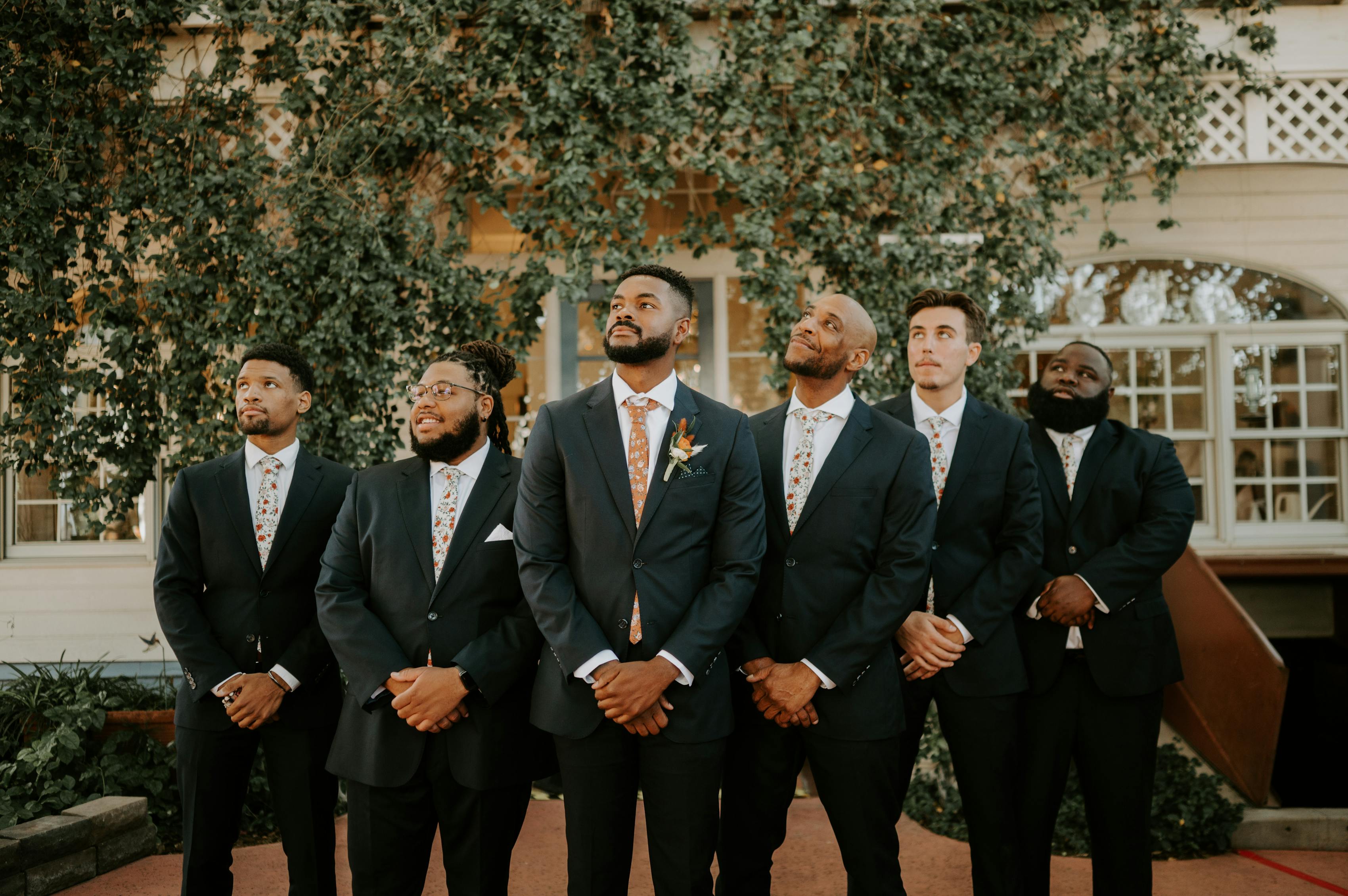 Serious face groomsmen of different heights wearing charcoal grey suits and floral ties