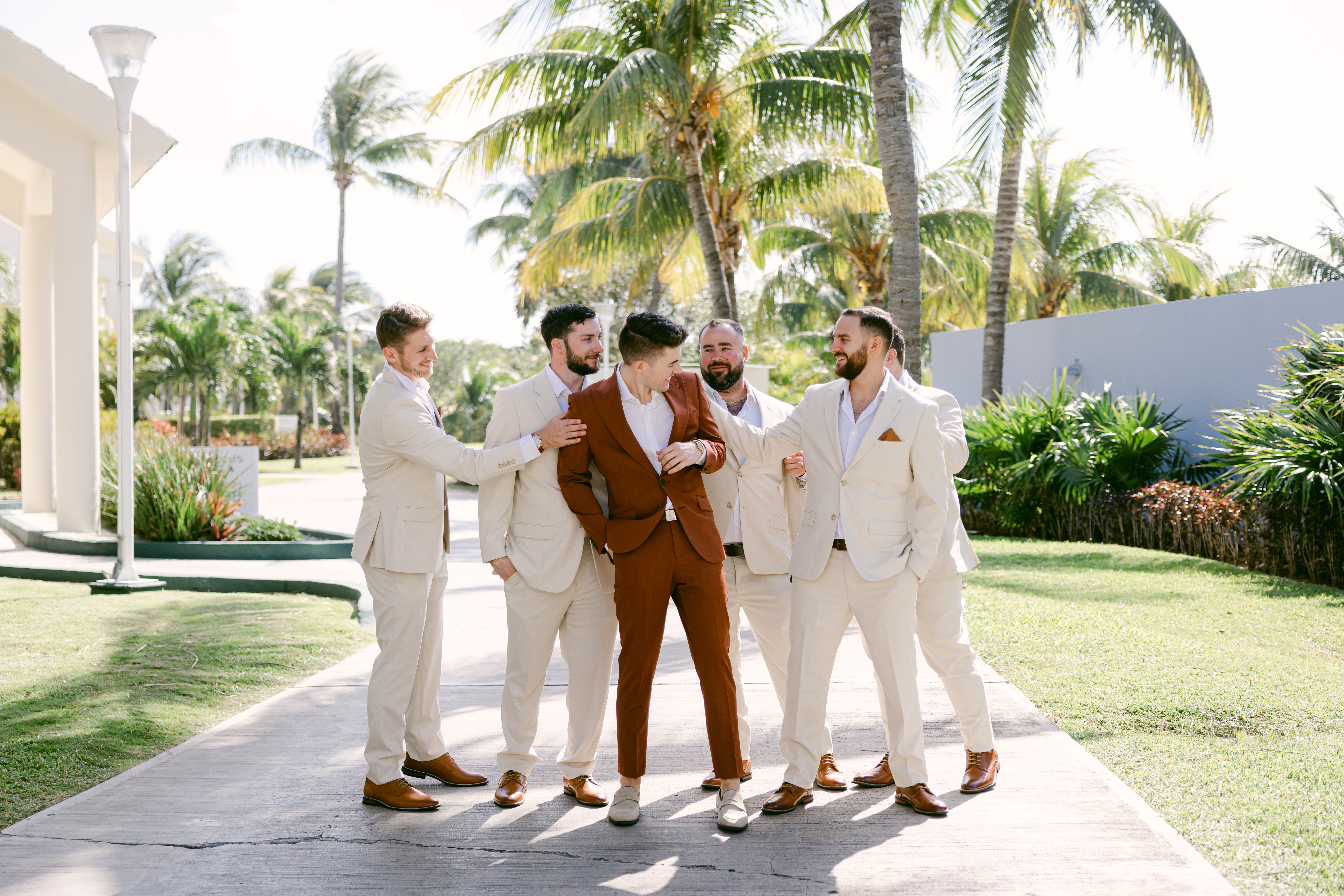 Groomsmen wearing tan suits for beach wedding with groom in terracotta clay suit