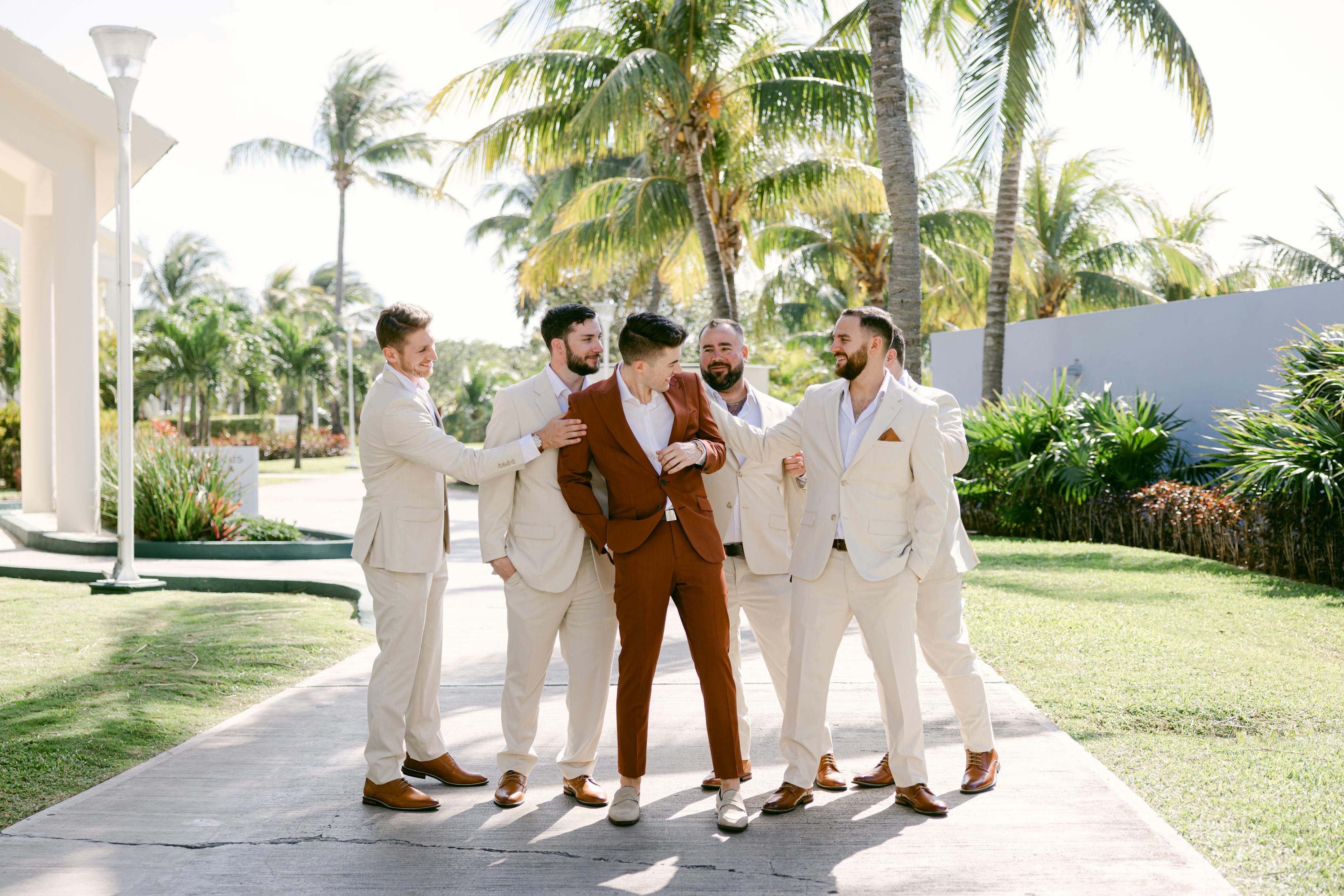 Groomsmen wearing tan suits for beach wedding with groom in terracotta clay suit