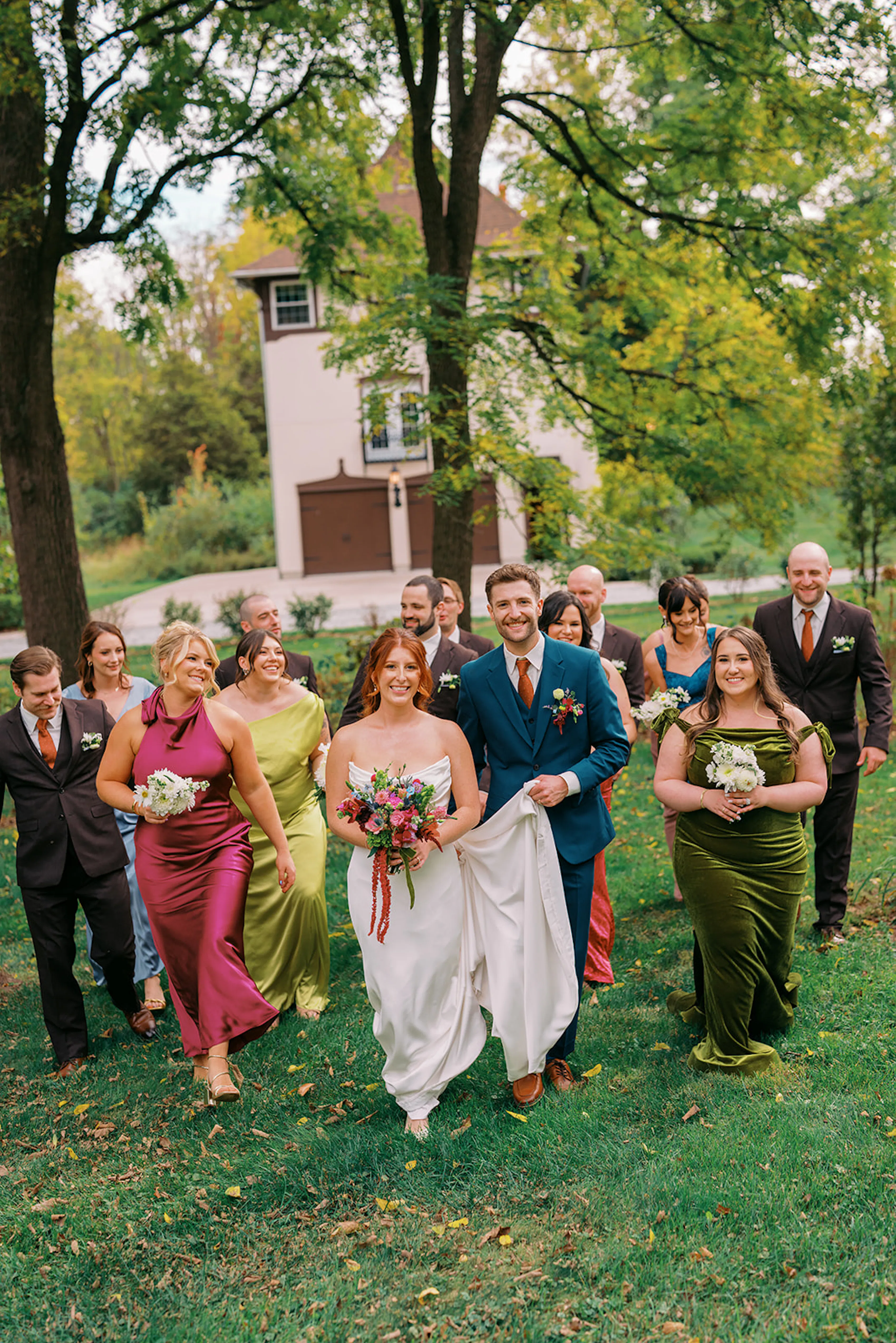 Colorful fall bridal party in pink, green, and chartreuse dresses with teal and dark brown suits