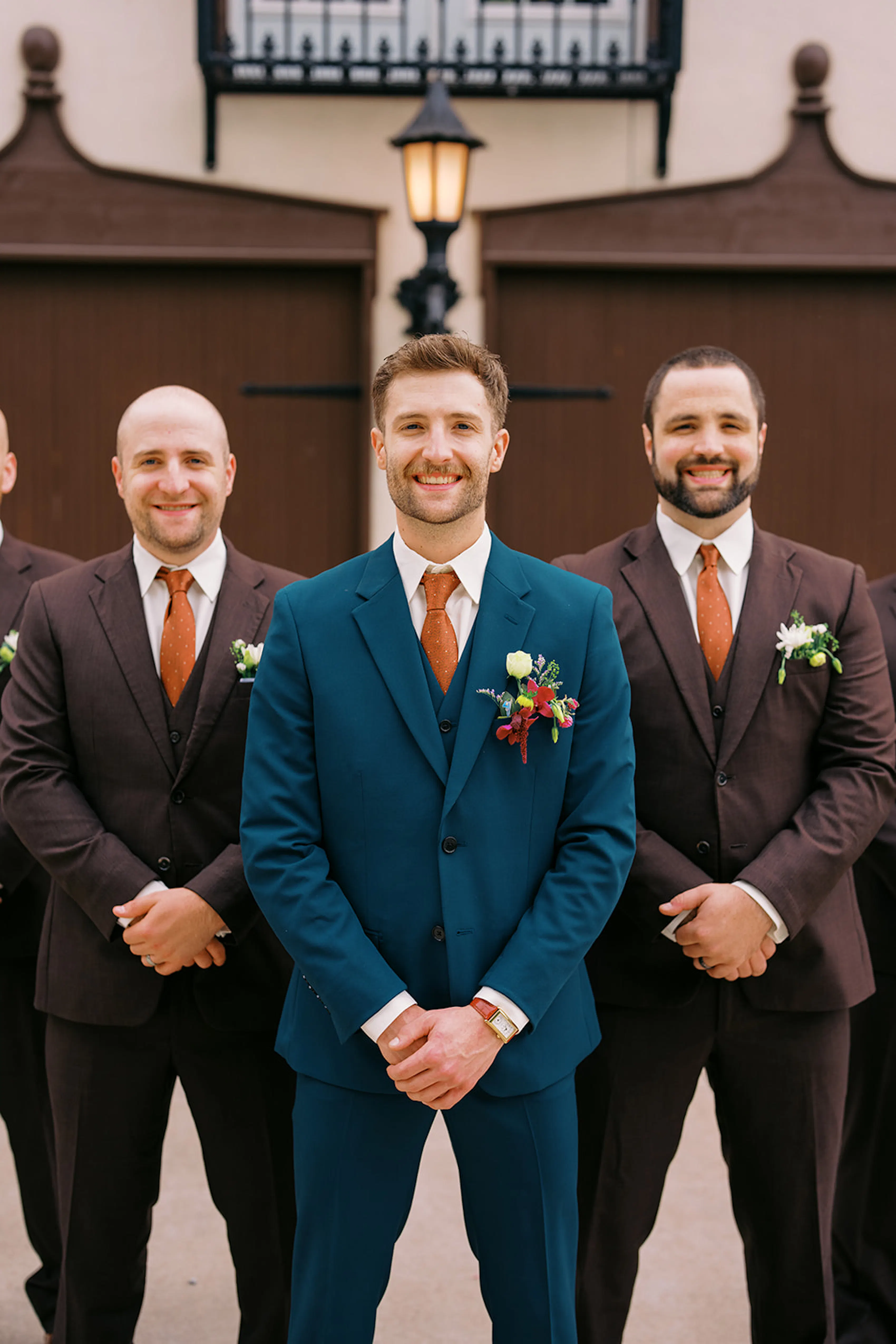 Groom wearing teal suit with groomsmen in dark brown suits and orange ties
