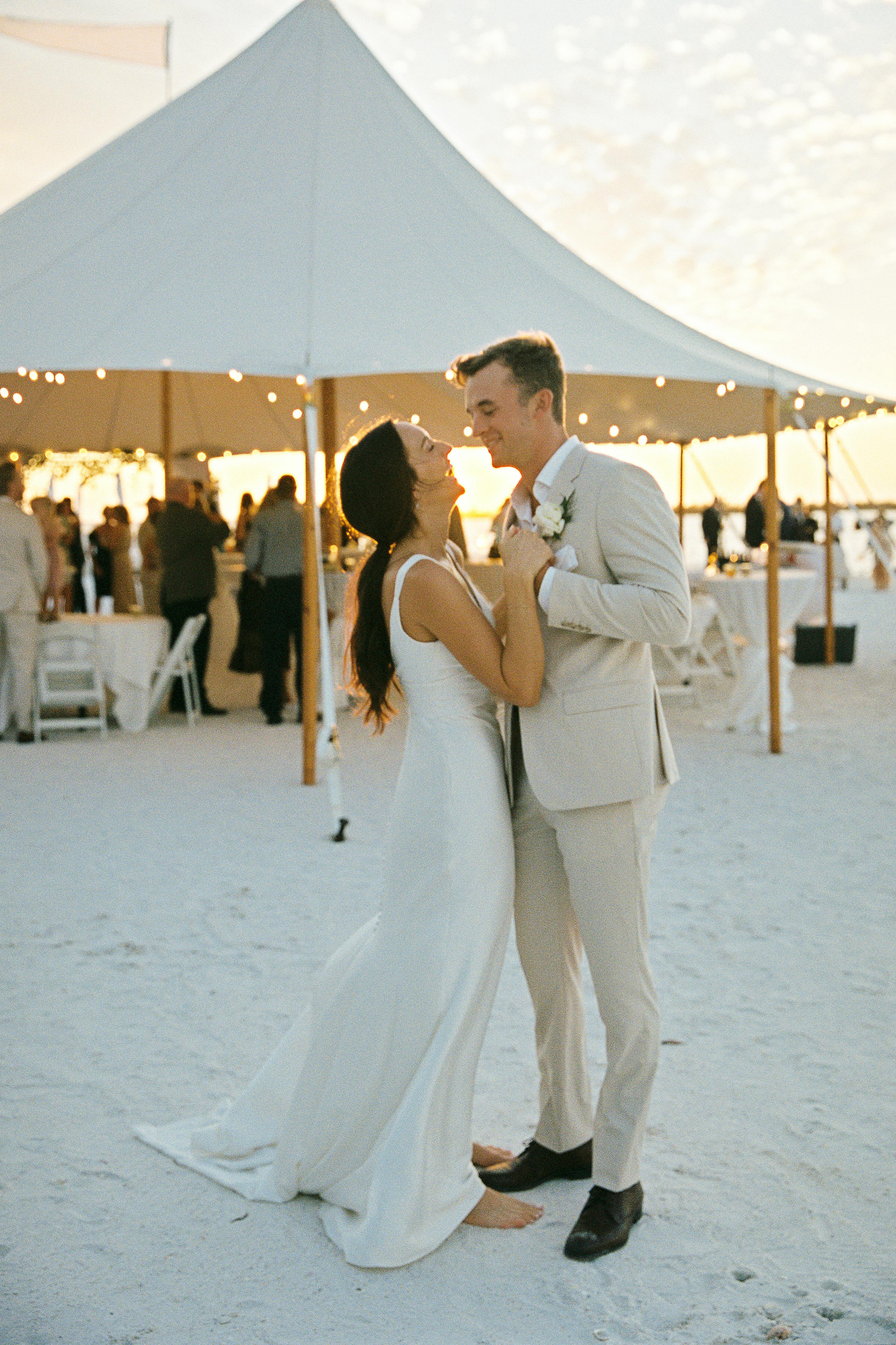 Relaxed beach wedding with tan suit for groom, wedding dress, tent, and twinkle lights