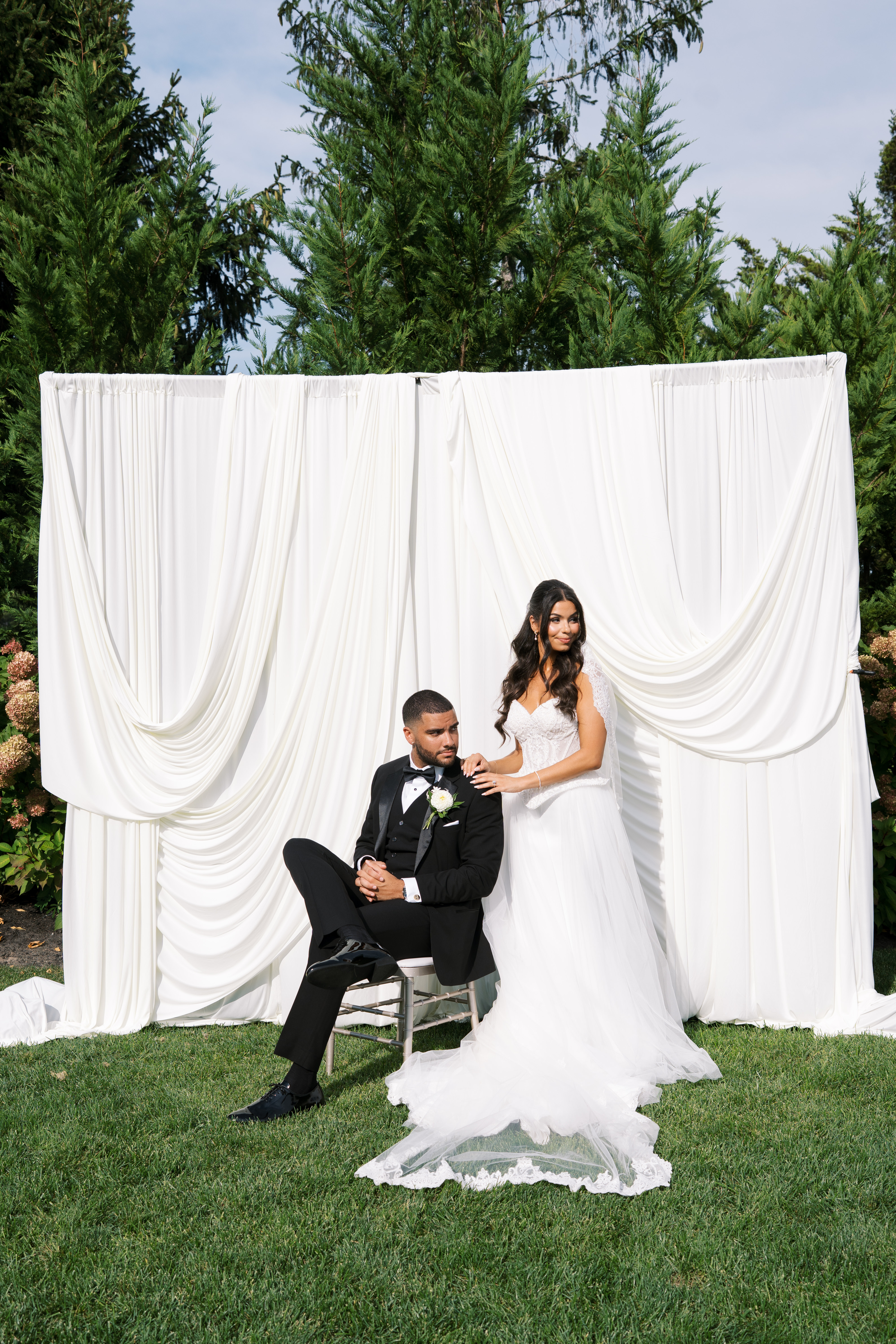 Black tie bride and groom wearing gown and tuxedo in front of white draped fabric backdrop