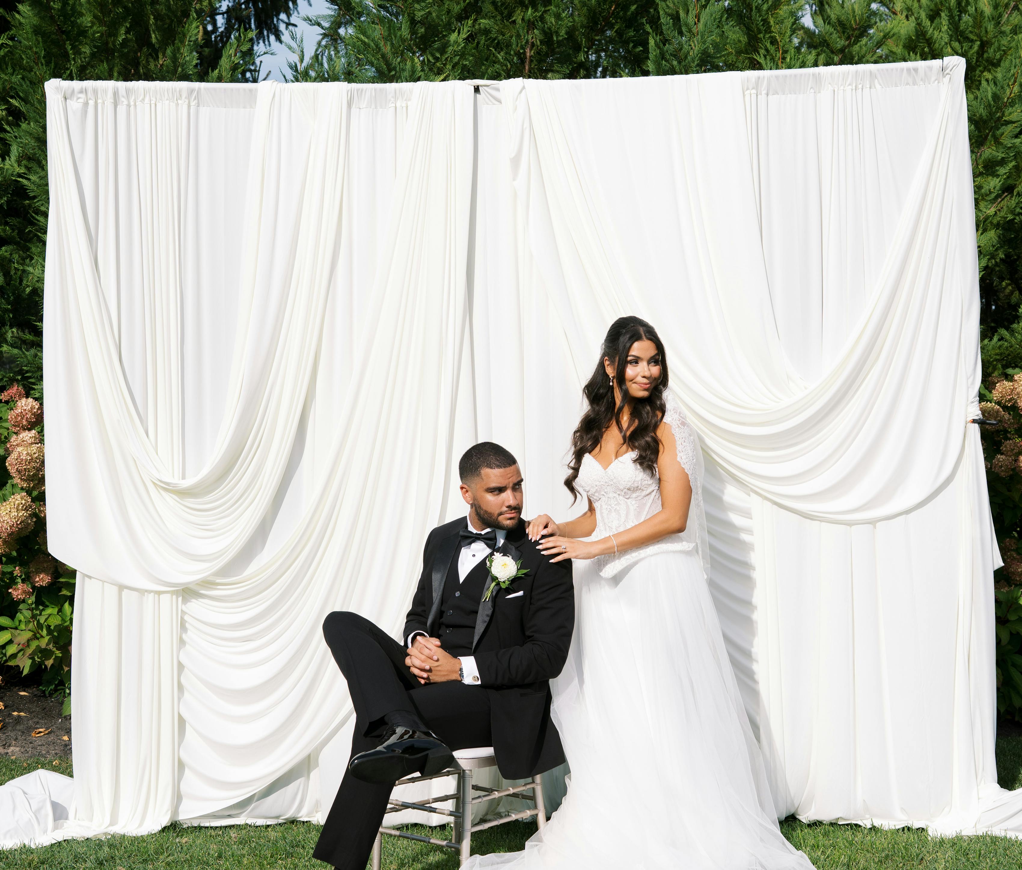 Black tie bride and groom wearing gown and tuxedo in front of white draped fabric backdrop