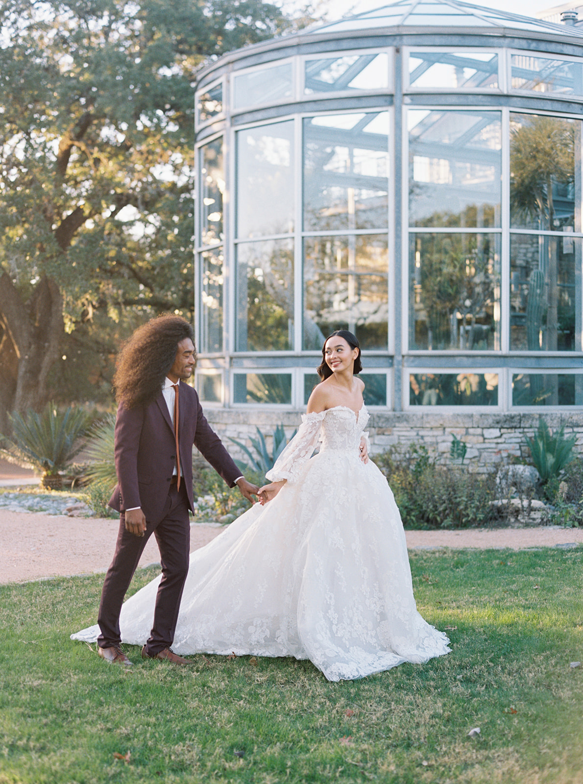 Bride in lace long sleeve dress and groom in burgundy suit at greenhouse wedding venue