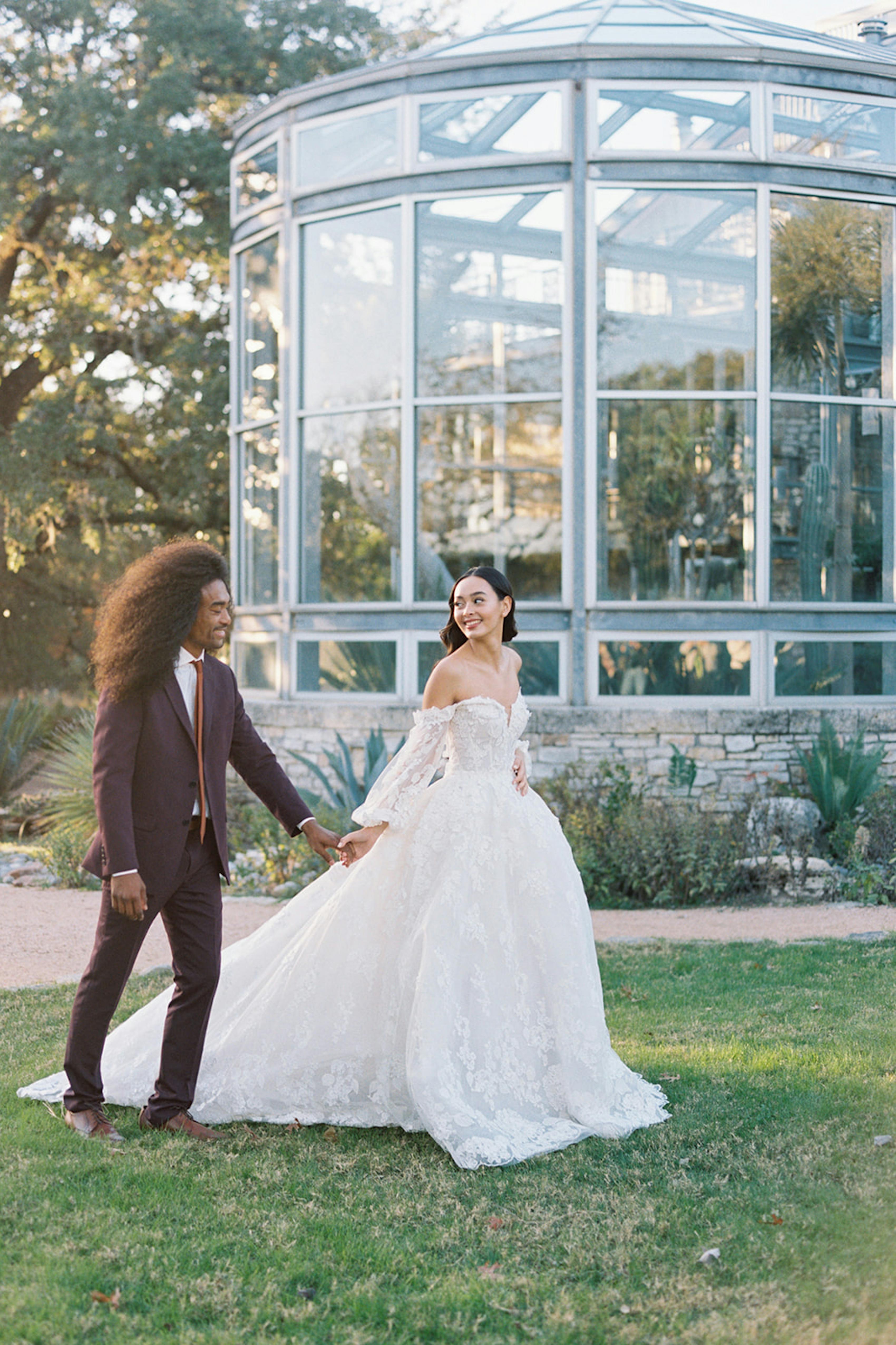 Bride in lace long sleeve dress and groom in burgundy suit at greenhouse wedding venue