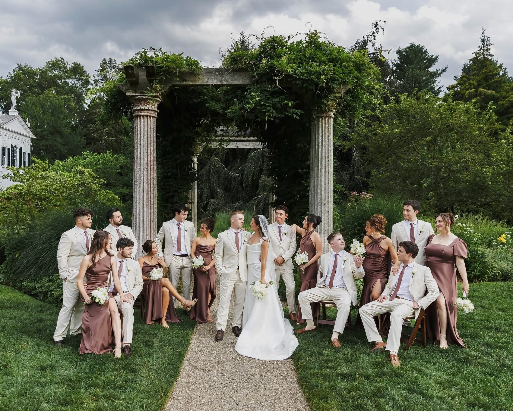 Outdoor wedding with tan groomsmen suits and coordinating dark brown satin bridesmaid dresses.