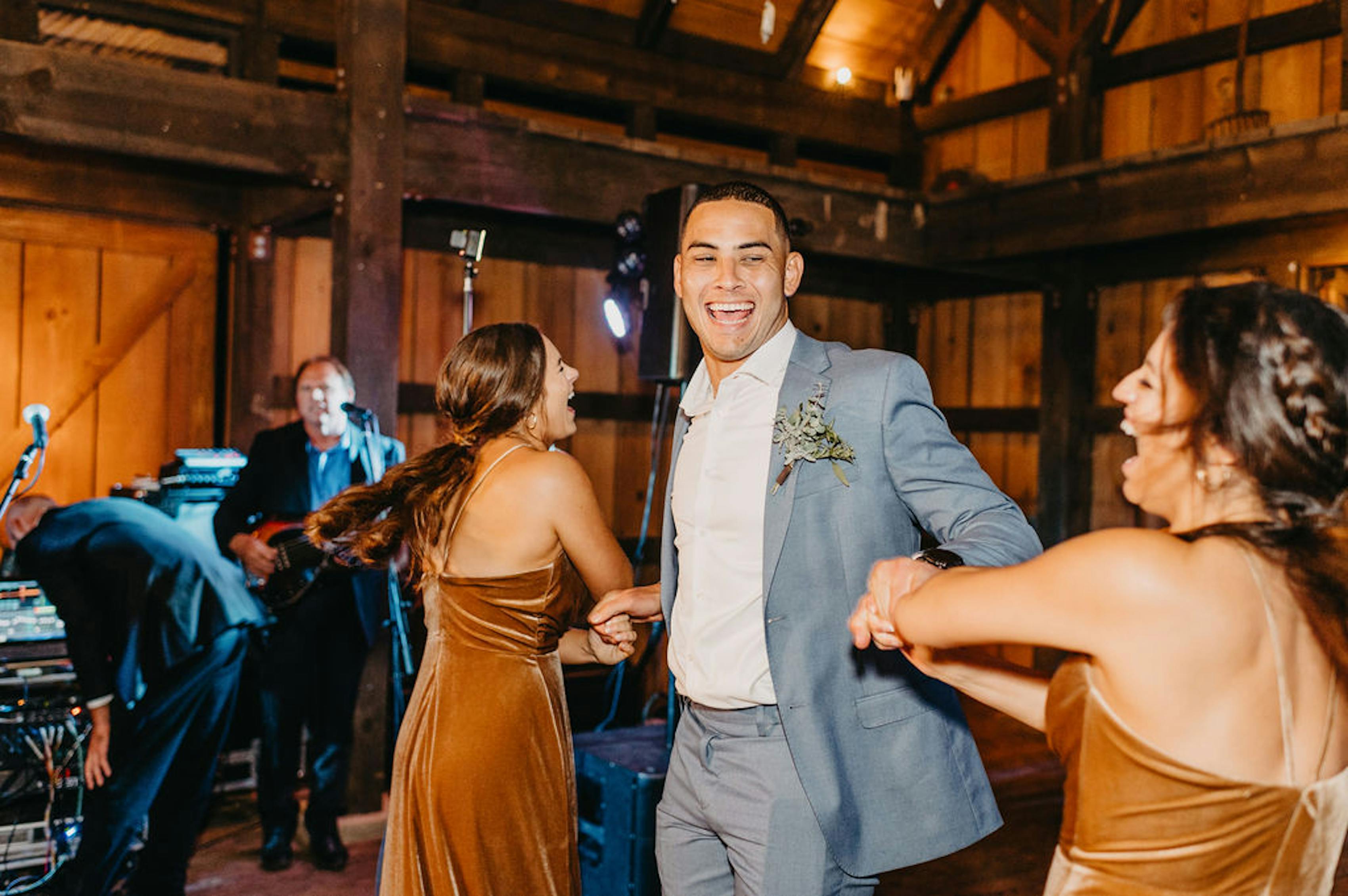 Bridesmaids wearing brown velvet dresses dancing with groomsman in light blue suit at barn wedding