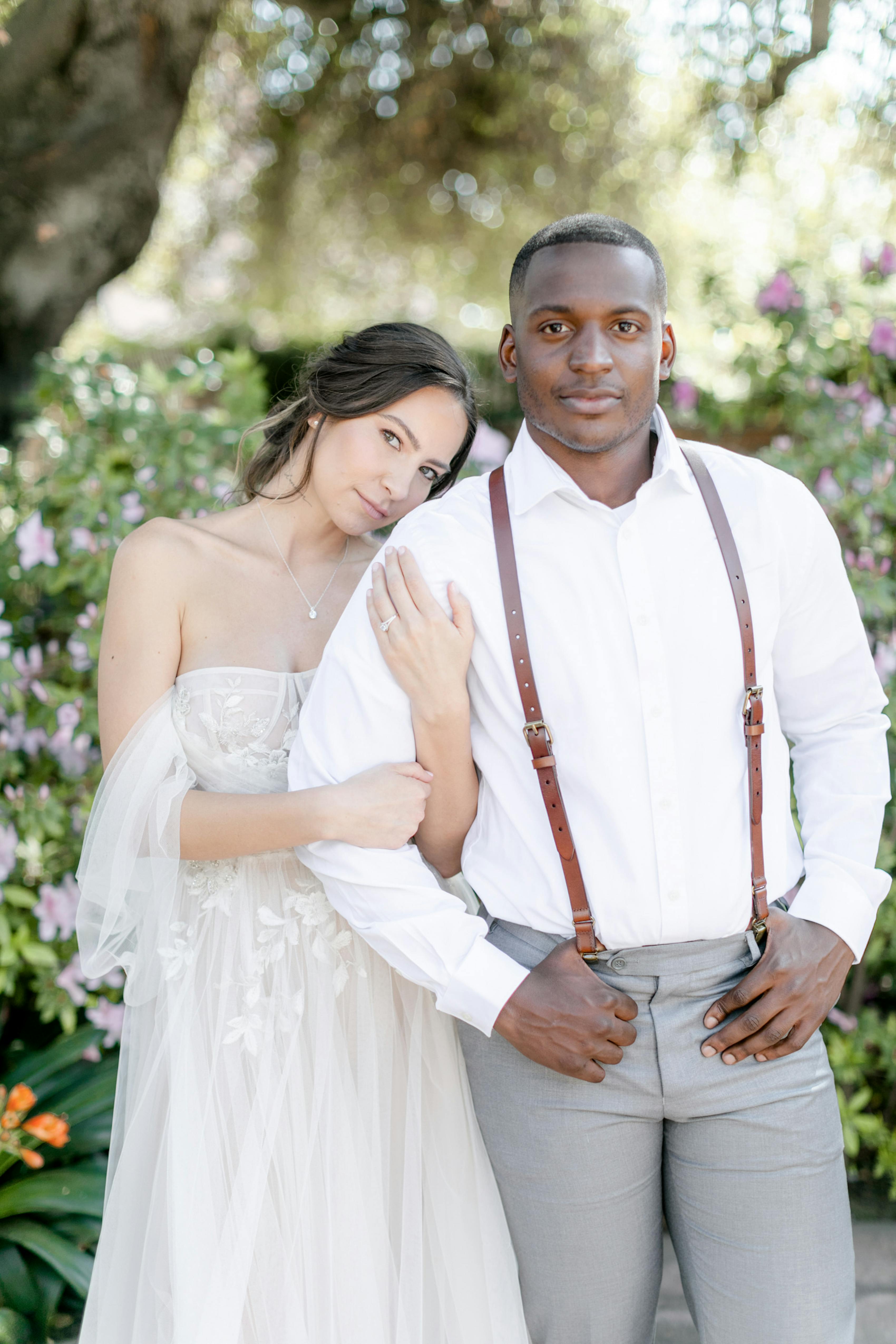 Bride in champagne boho gown leaning on groom wearing brown leather suspenders and grey pants