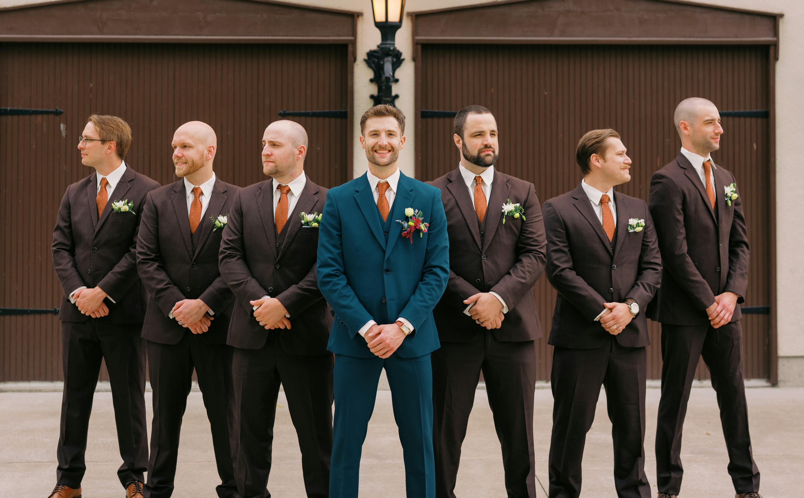 Groom wearing teal suit with groomsmen wearing dark brown suits and rust ties