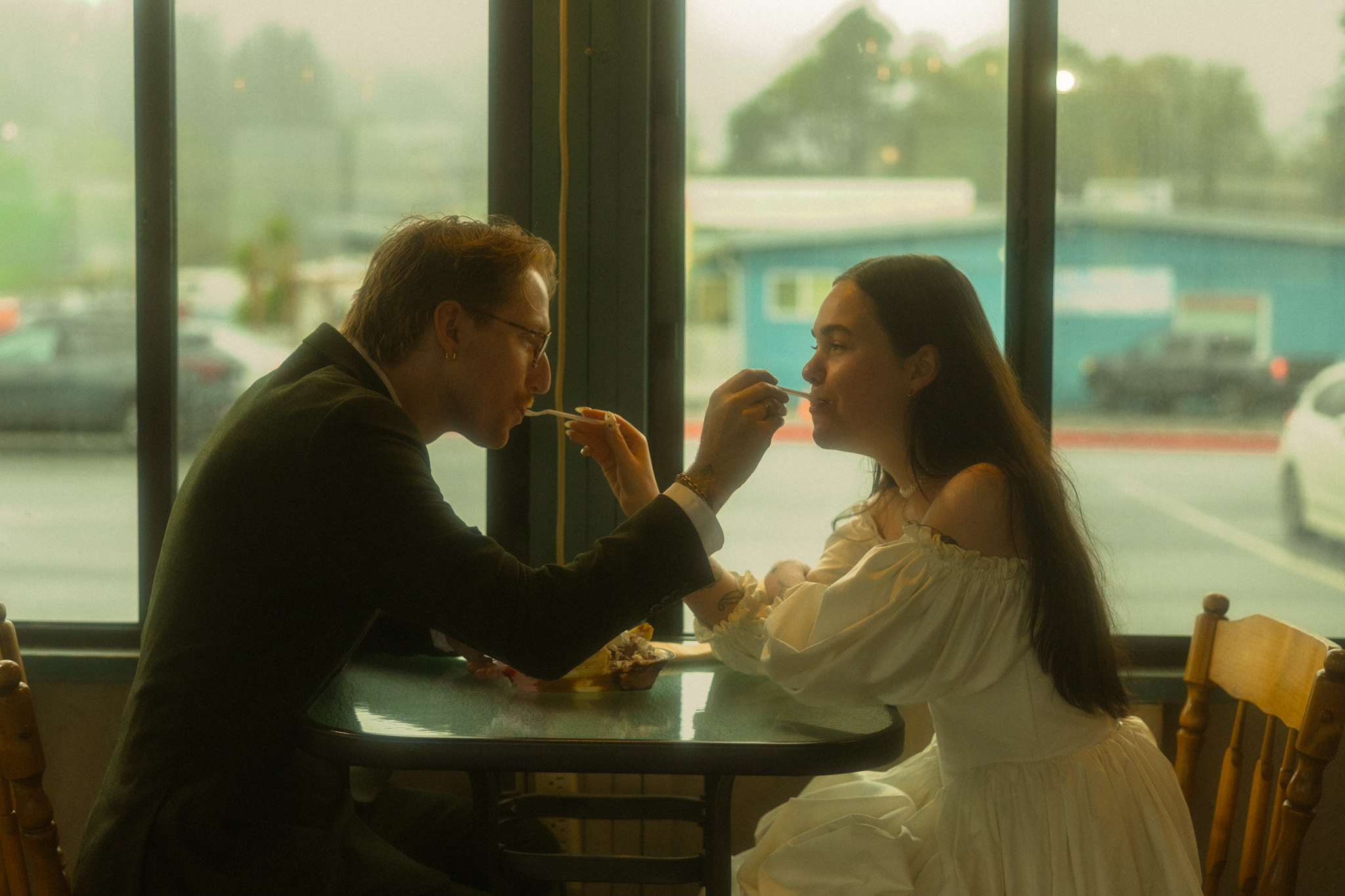 Dressed up couple wearing suit and gown in country diner feeding each other french fries