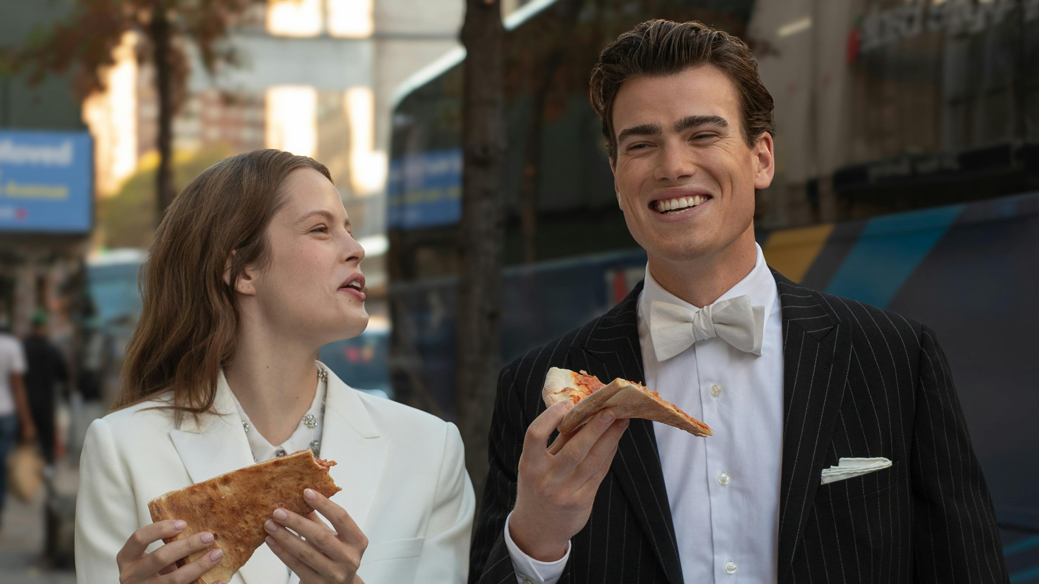 Casual newlyweds walking around city wearing pinstripe groom's suit and bridal suit eating pizza