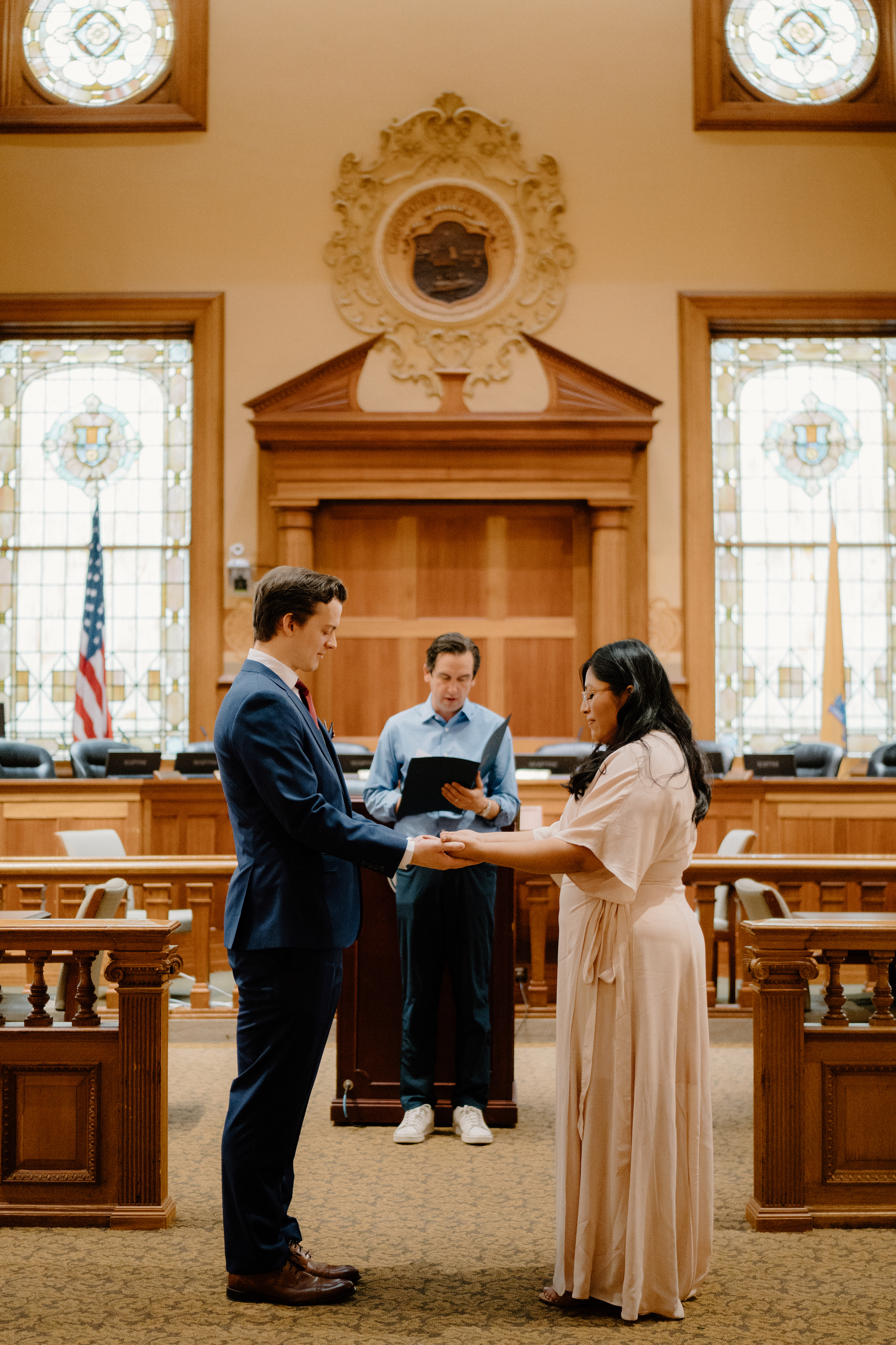 Couple during courthouse wedding ceremony getting married wearing cream dress and navy suit