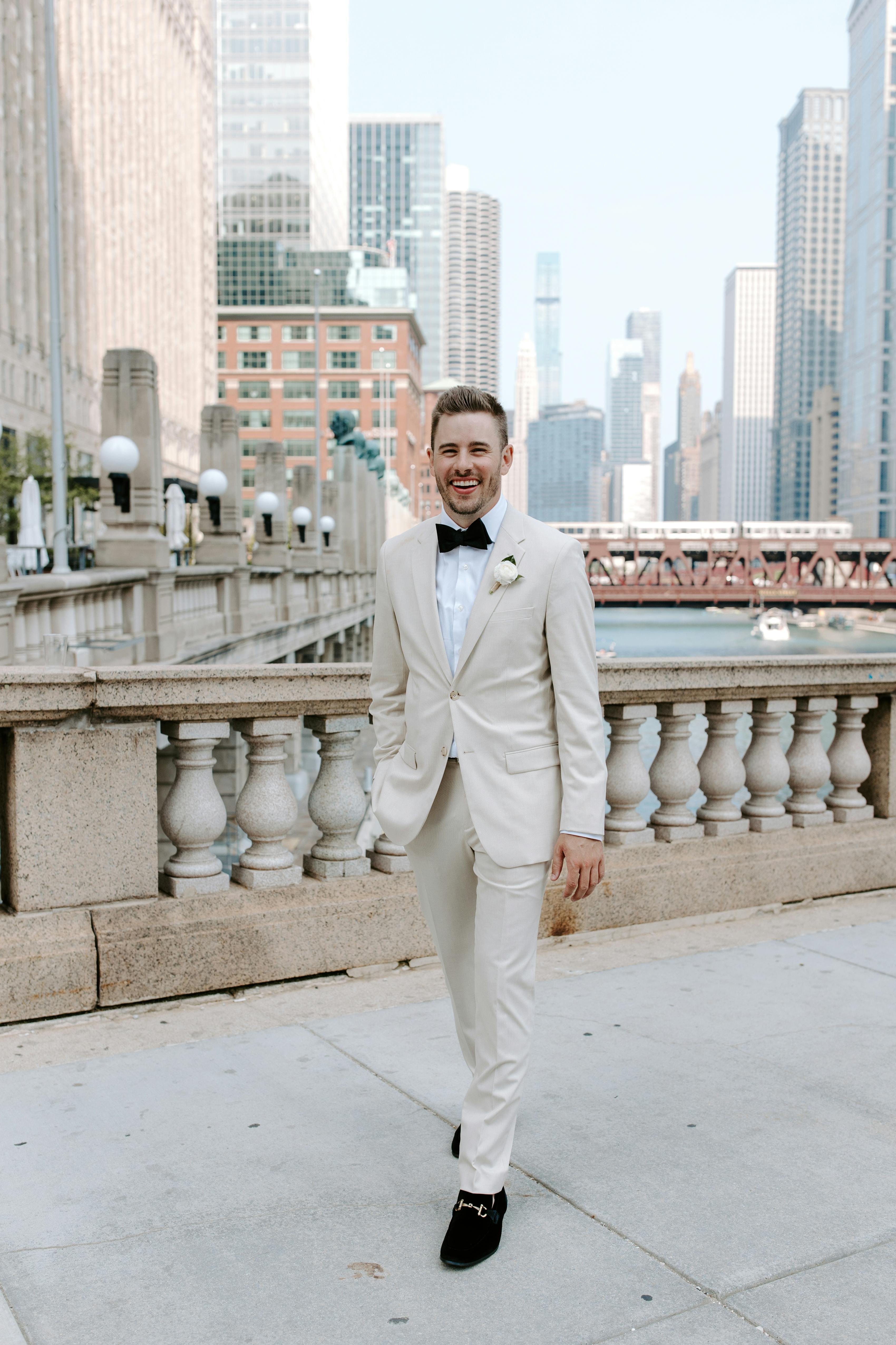 Groom outside courthouse wearing light tan wedding suit with black bow tie