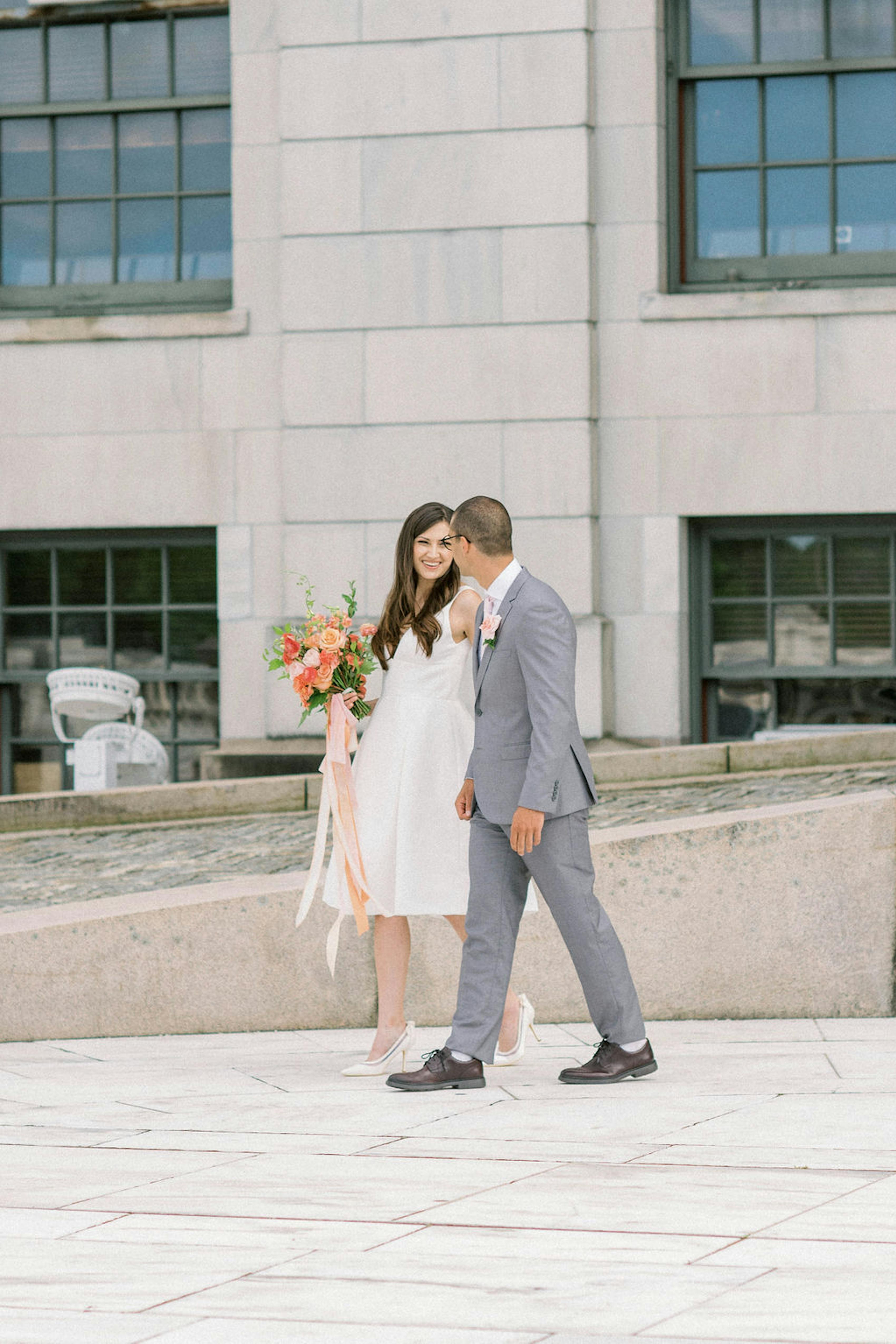 Bride and groom walking after courthouse spring wedding in short dress and light grey suit